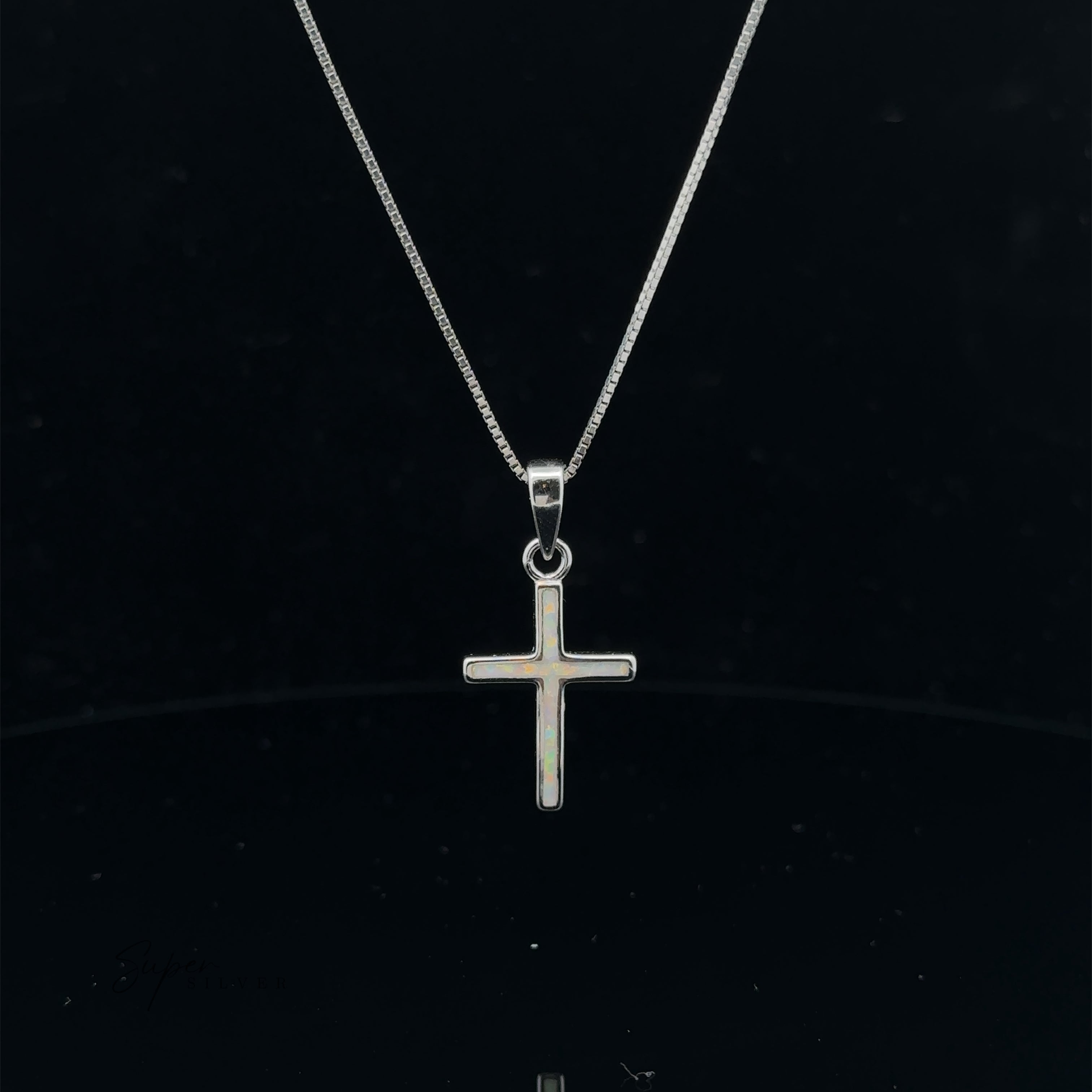 The Lab-Created Opal Cross Pendant gracefully suspended on a delicate chain against a black background showcases the enduring appeal of sterling silver jewelry.