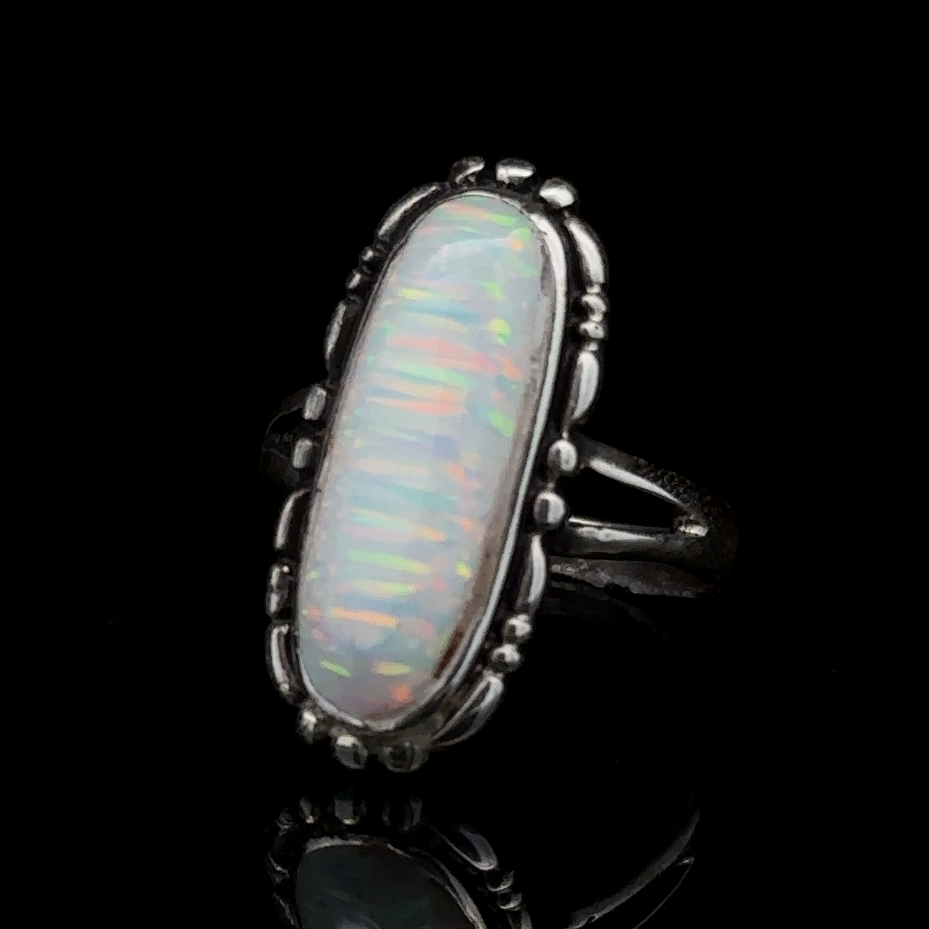 A sterling silver ring featuring an elongated, lab-created opal gemstone with iridescent colors, placed against a black background.
Adjusted Sentence: An American Made Oval Opal Ring featuring an elongated, lab-created opal gemstone with iridescent colors, placed against a black background.