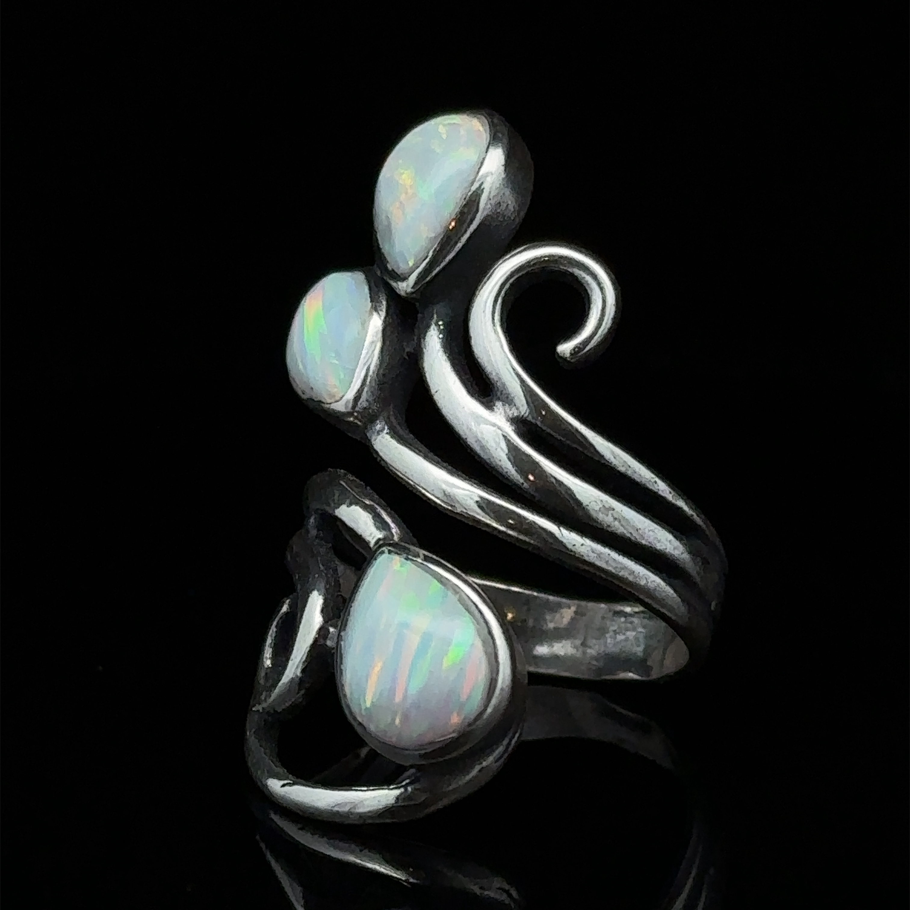 A Stunning Wrap-Around Opal Ring featuring three white opal stones set in a swirling design against a black background.
