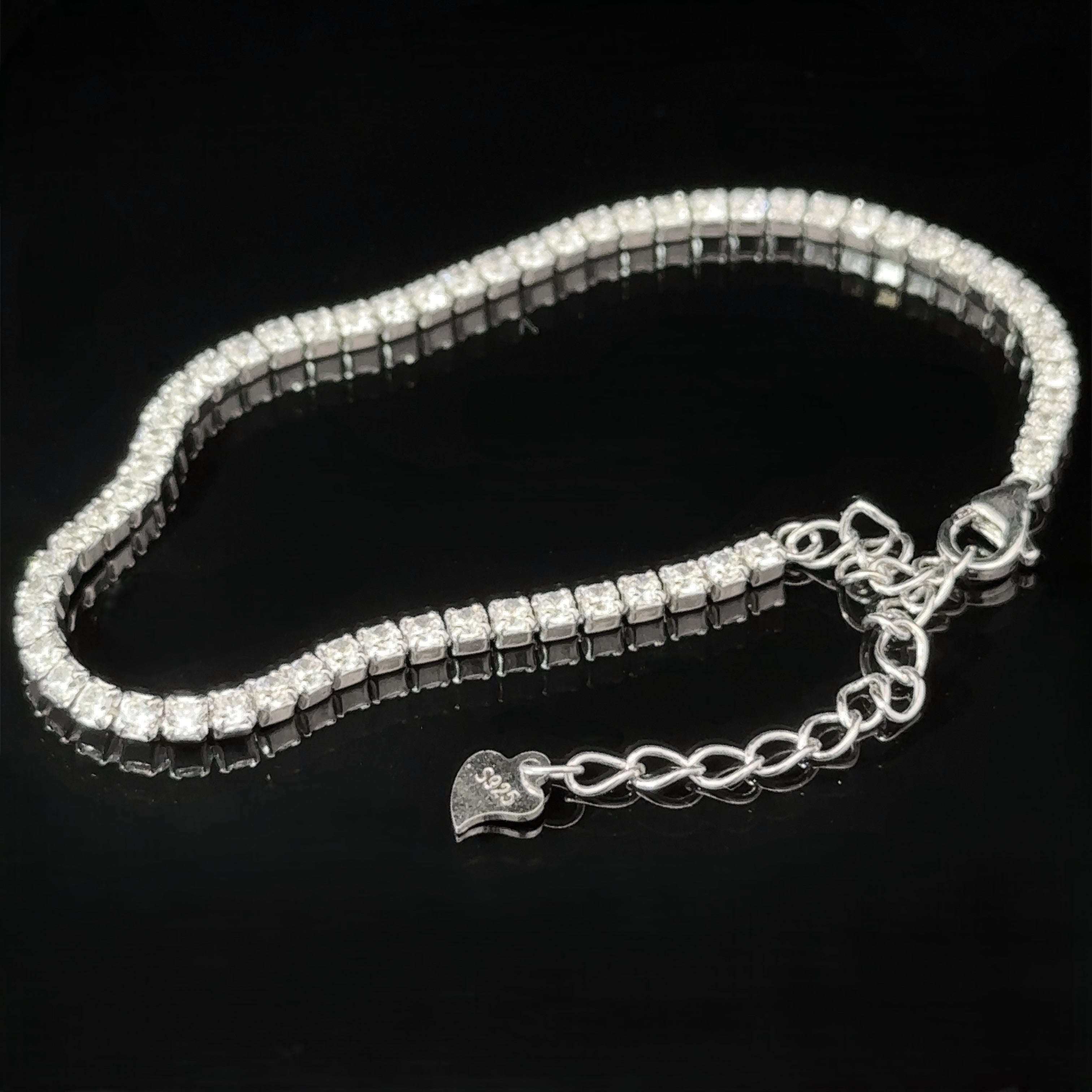 A Square Cubic Zirconia Tennis Bracelet featuring a row of square-cut cubic zirconia crystals and a heart-shaped charm on the rhodium-plated sterling silver chain, displayed against a black background.