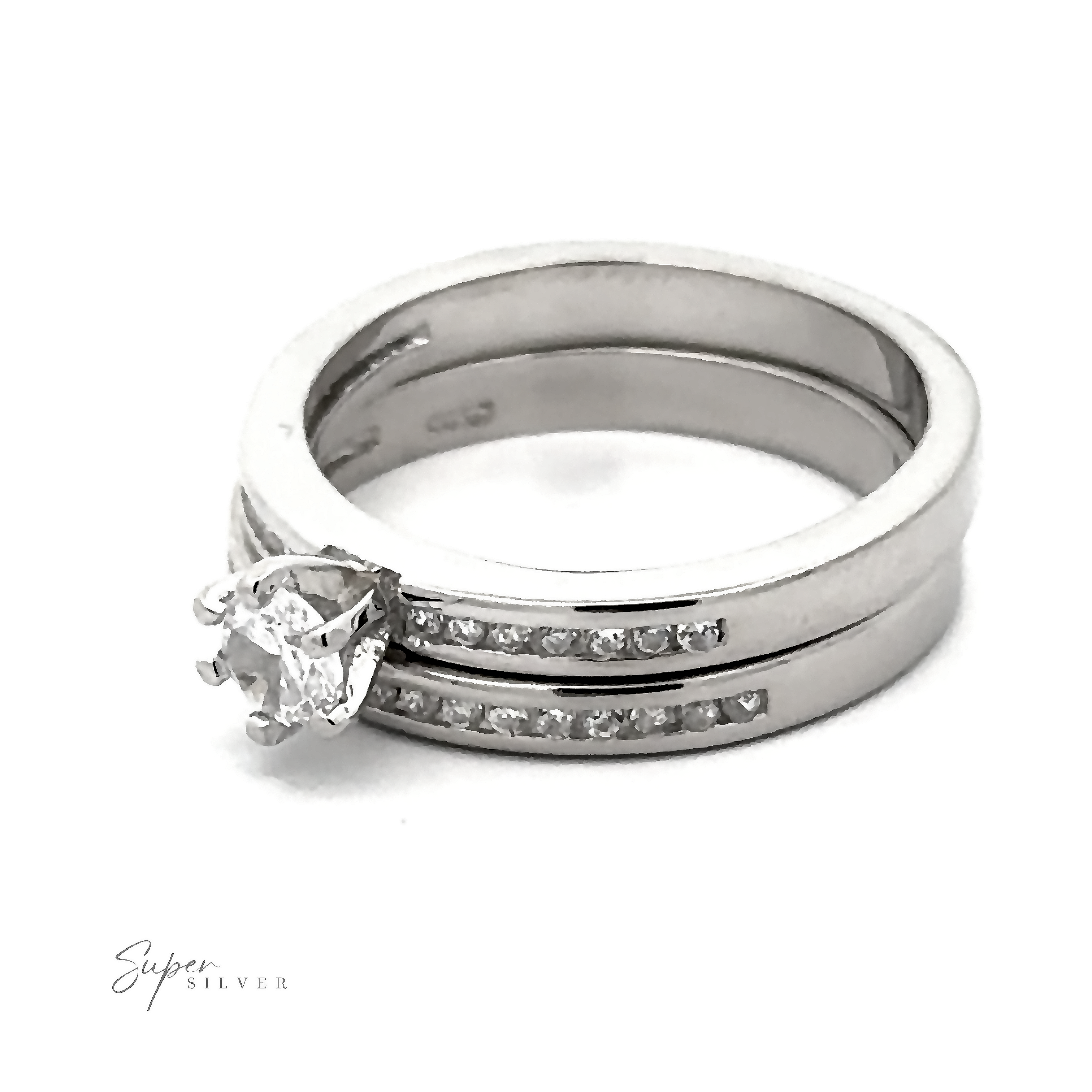 A Brilliant Round Cubic Zirconia Wedding Ring Set with a prominent round diamond and a matching wedding band featuring small embedded diamonds, both marked "Super Silver," boast a Sterling Silver Rhodium Finish for added shine.