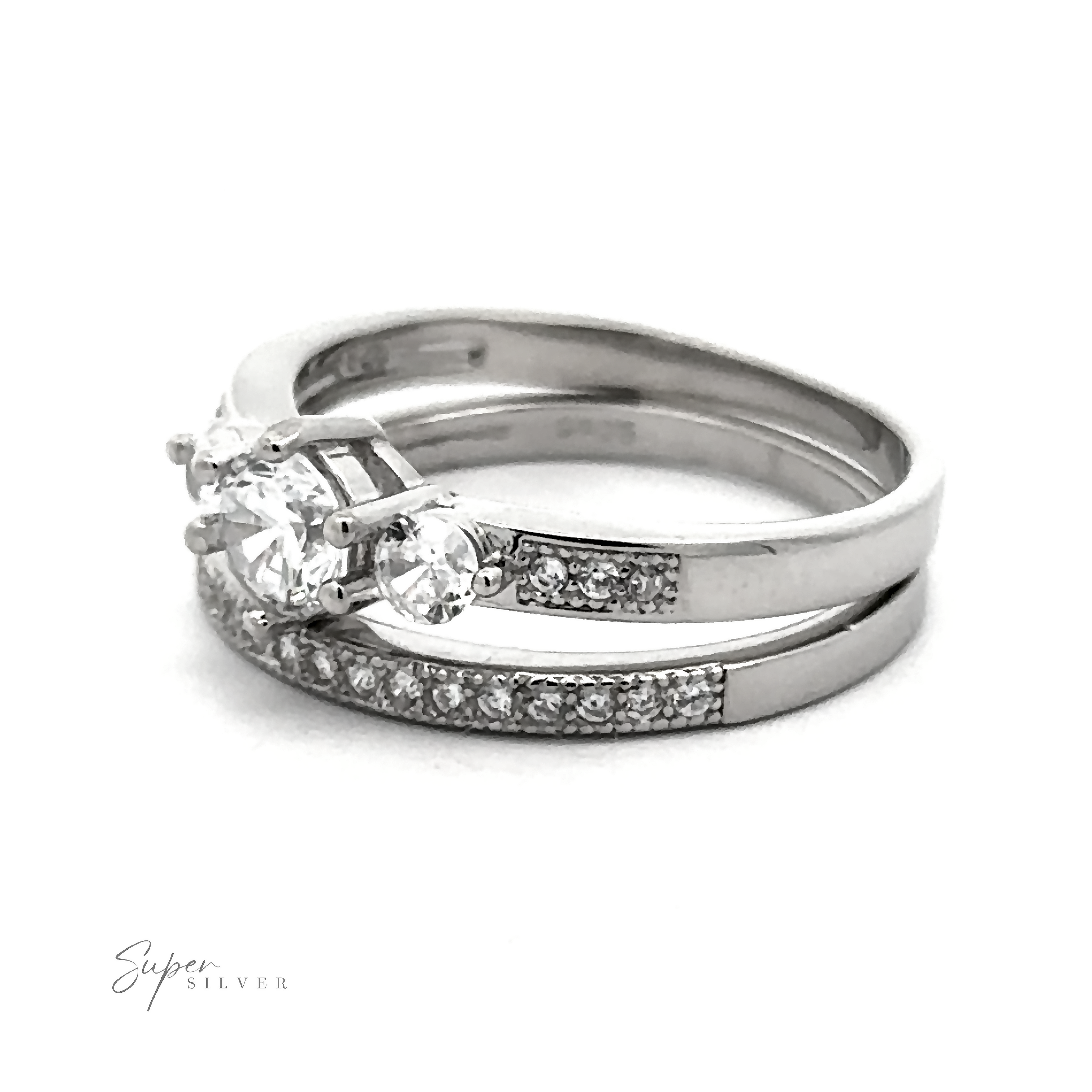 A set of two silver rings, one featuring three large round-cut high-quality cubic zirconia stones and the other adorned with smaller gemstones along the band. This Round Cubic Zirconia Wedding Band Set is displayed on a white background.