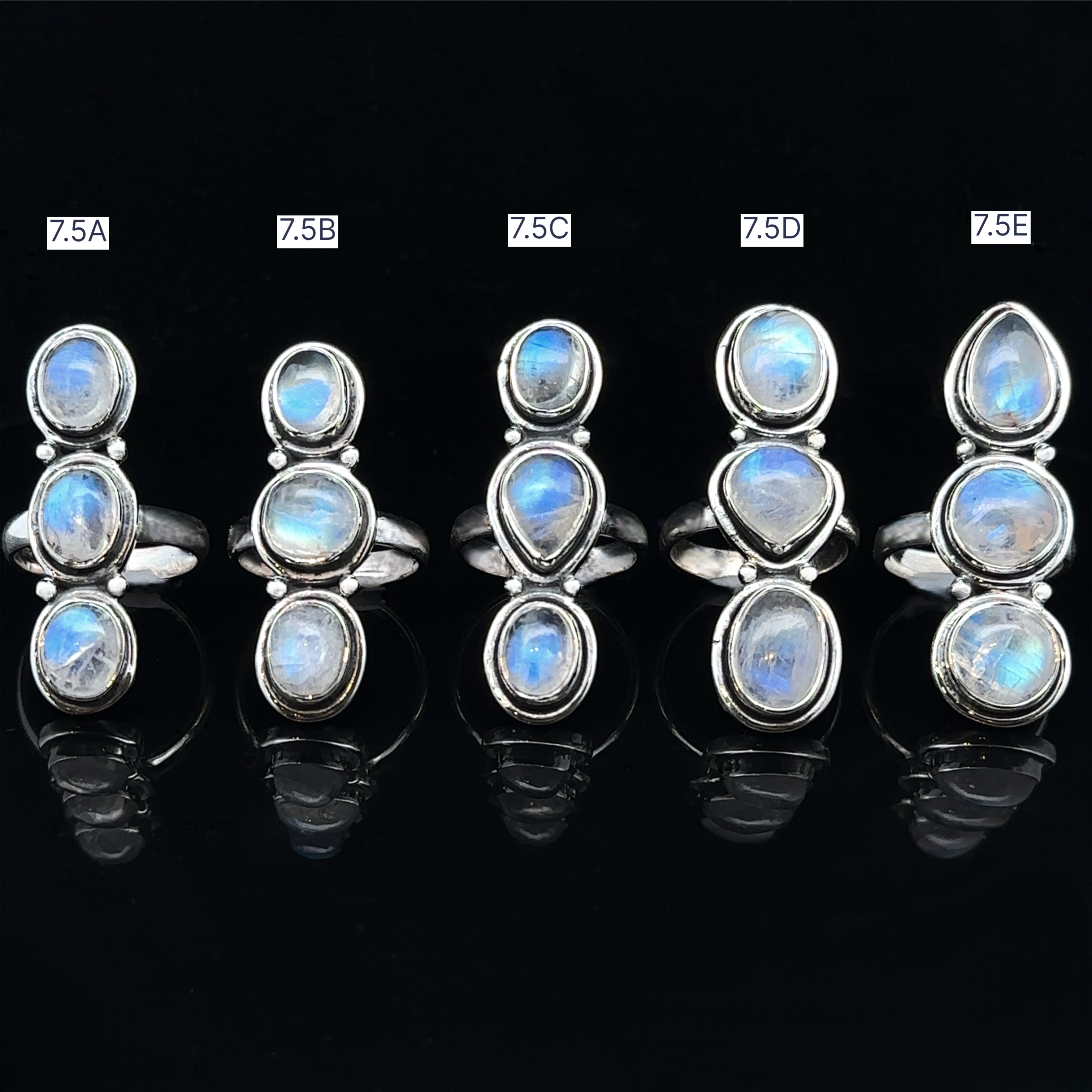 Five Triple Moonstone Rings with blue gemstones, labeled 7.5A to 7.5E, are elegantly displayed on a black background, each emanating a unique goddess energy.