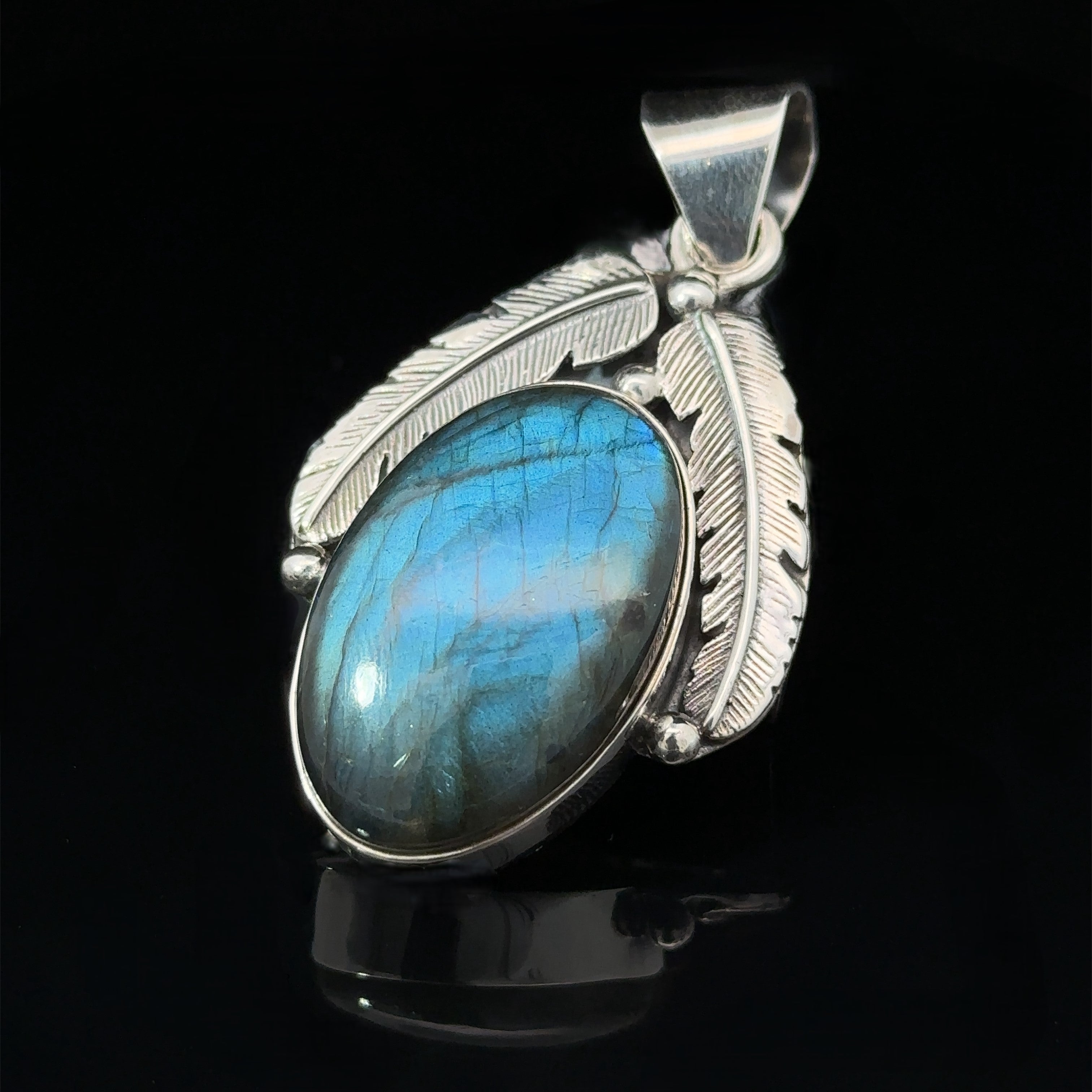 A Beautiful Southwest Stone Pendant featuring a mesmerizing blue labradorite stone is adorned with detailed feather designs on a black background.