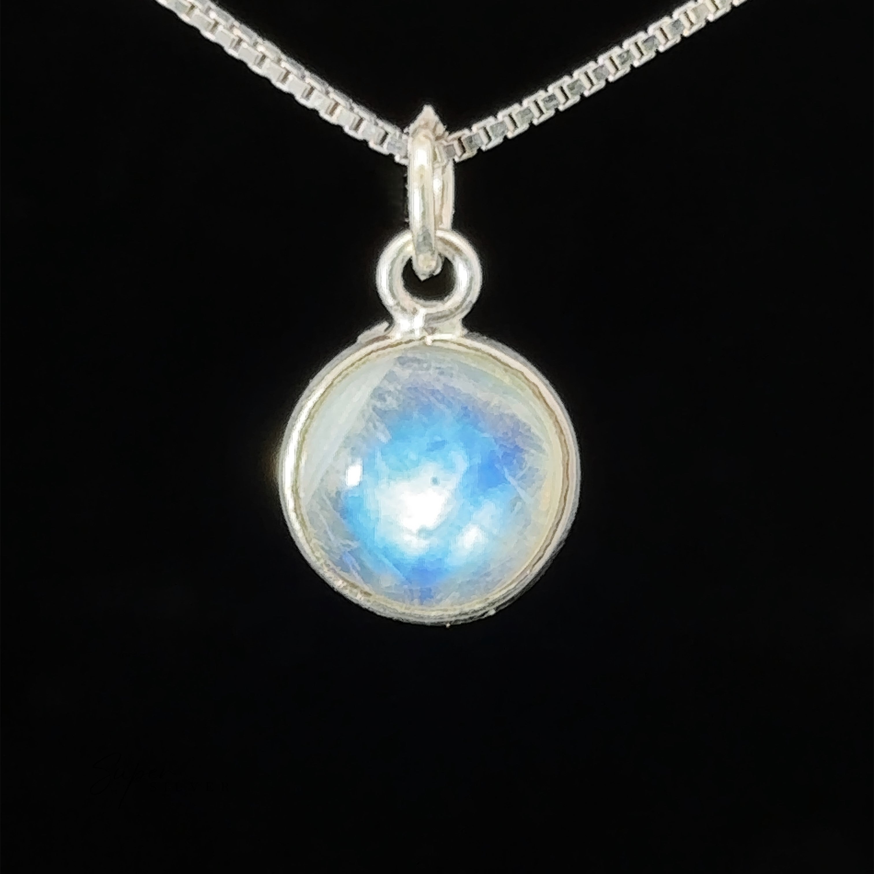 A Simple and Dainty Moonstone Pendant showcasing a round, iridescent moonstone set against a black background, with an intricate wire wrapped design.