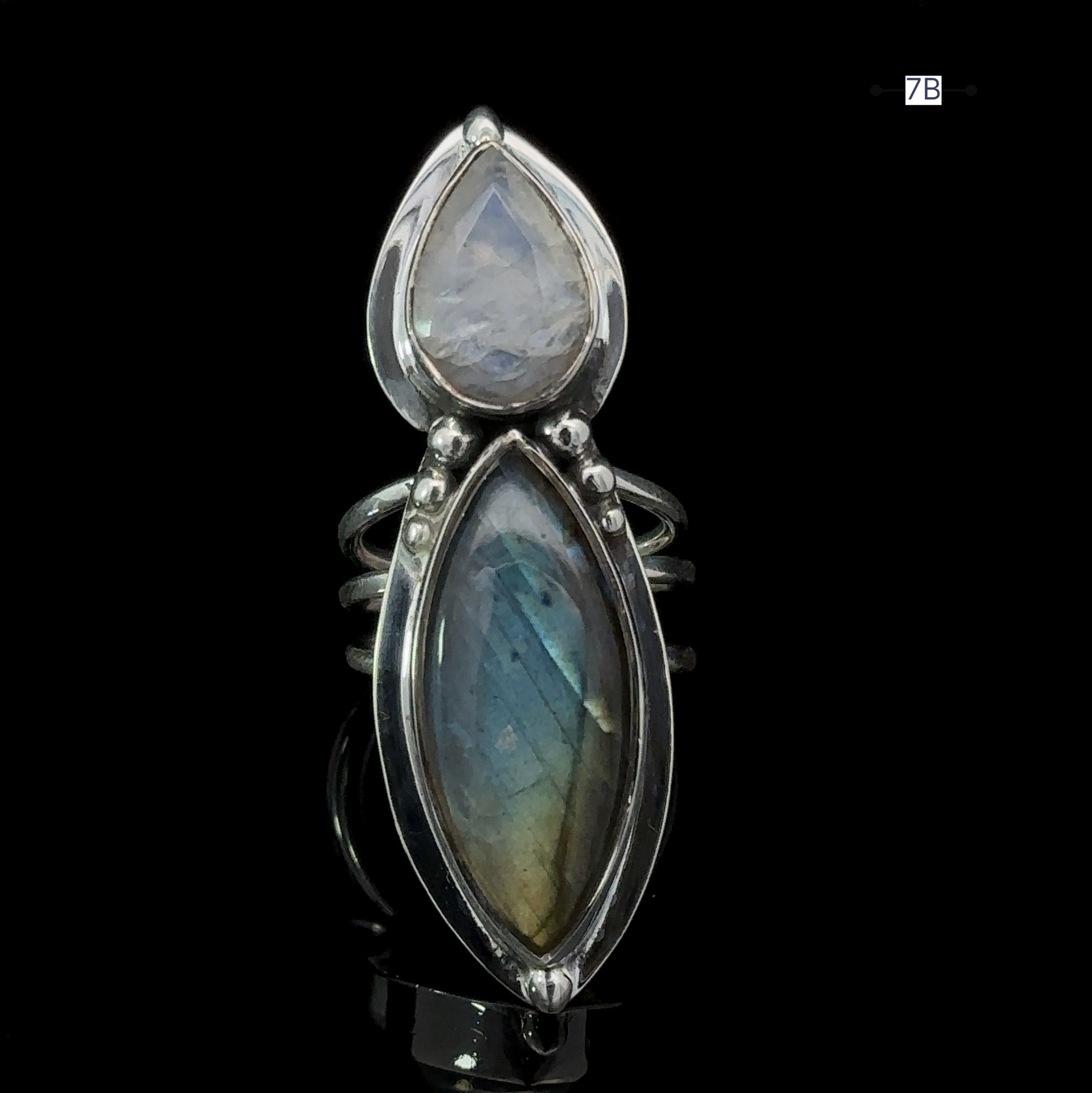 Introducing the Heavy Labradorite And Moonstone Ring, a stunning silver statement piece featuring two teardrop-shaped gemstones. The top stone is a lighter moonstone, while the bottom boasts a mesmerizing blue-green hue, capturing the enchanting look of labradorite.