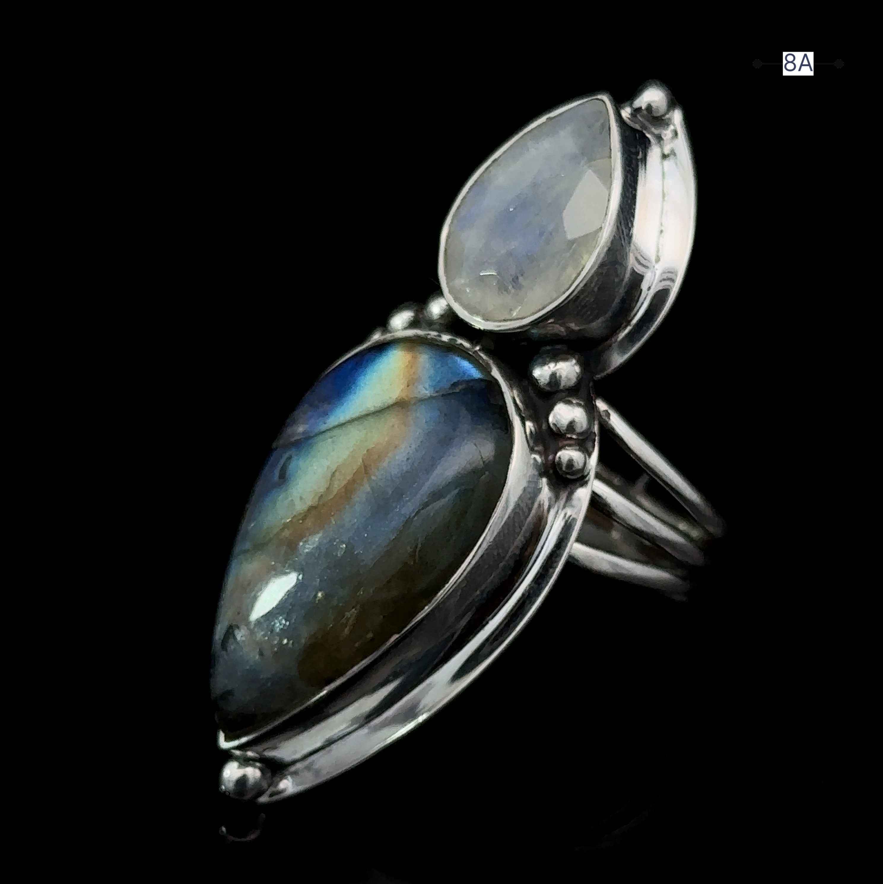 Product Description: Introducing the Heavy Labradorite and Moonstone Ring - a captivating accessory showcasing a large, teardrop-shaped labradorite and a smaller, oval-shaped moonstone, both set in a silver band against a striking black background.