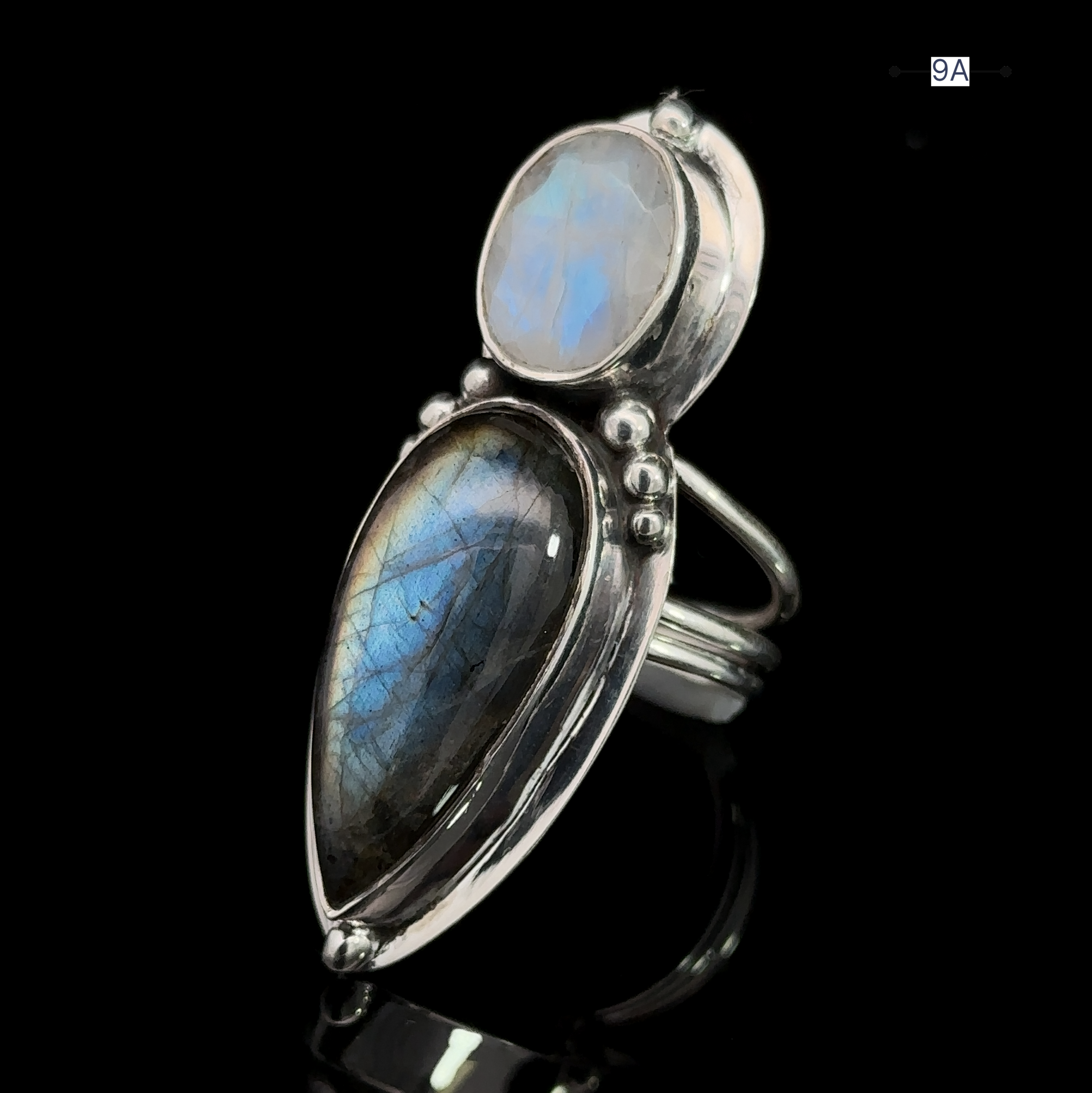The Heavy Labradorite and Moonstone Ring boasts a large, teardrop-shaped labradorite stone accented by a smaller round moonstone set above it, all beautifully displayed on a black reflective surface.