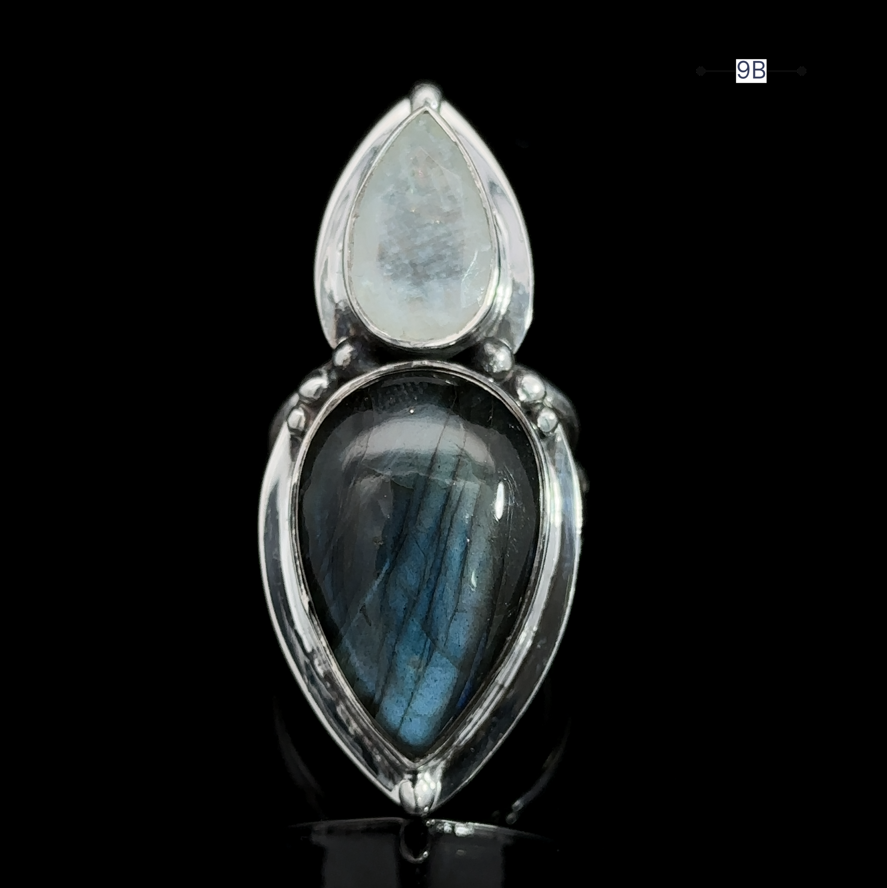 The Heavy Labradorite And Moonstone Ring is a stunning statement piece, featuring a silver band adorned with two tear-shaped stones: a smaller, translucent white moonstone and a larger, dark, iridescent blue-green labradorite.