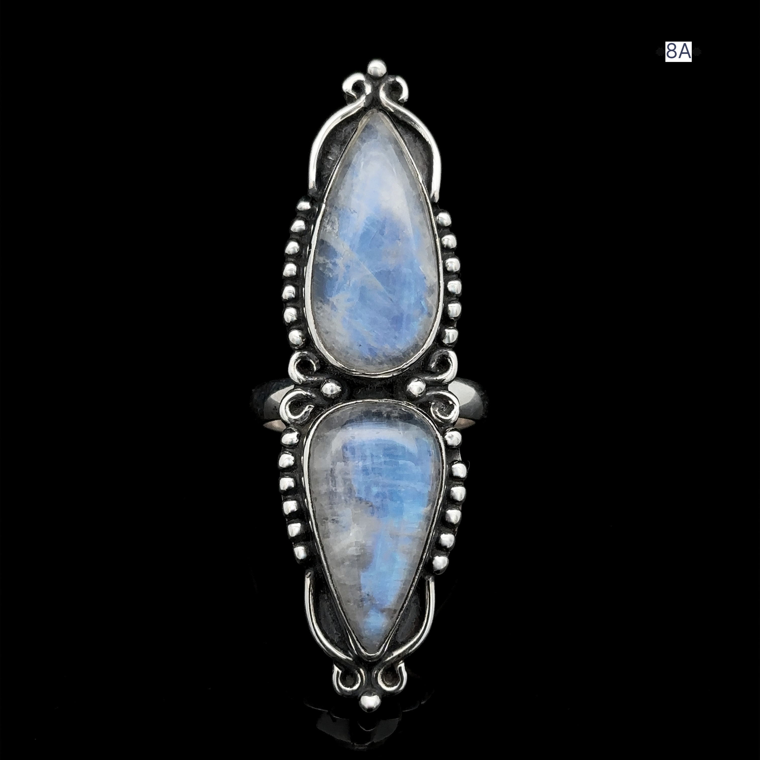 The Long Double Teardrop Moonstone Ring, crafted from sterling silver, features two vertically aligned, teardrop-shaped moonstones. Adorned with small silver beads around the edges and set against a black background, this statement ring exudes elegance and sophistication.