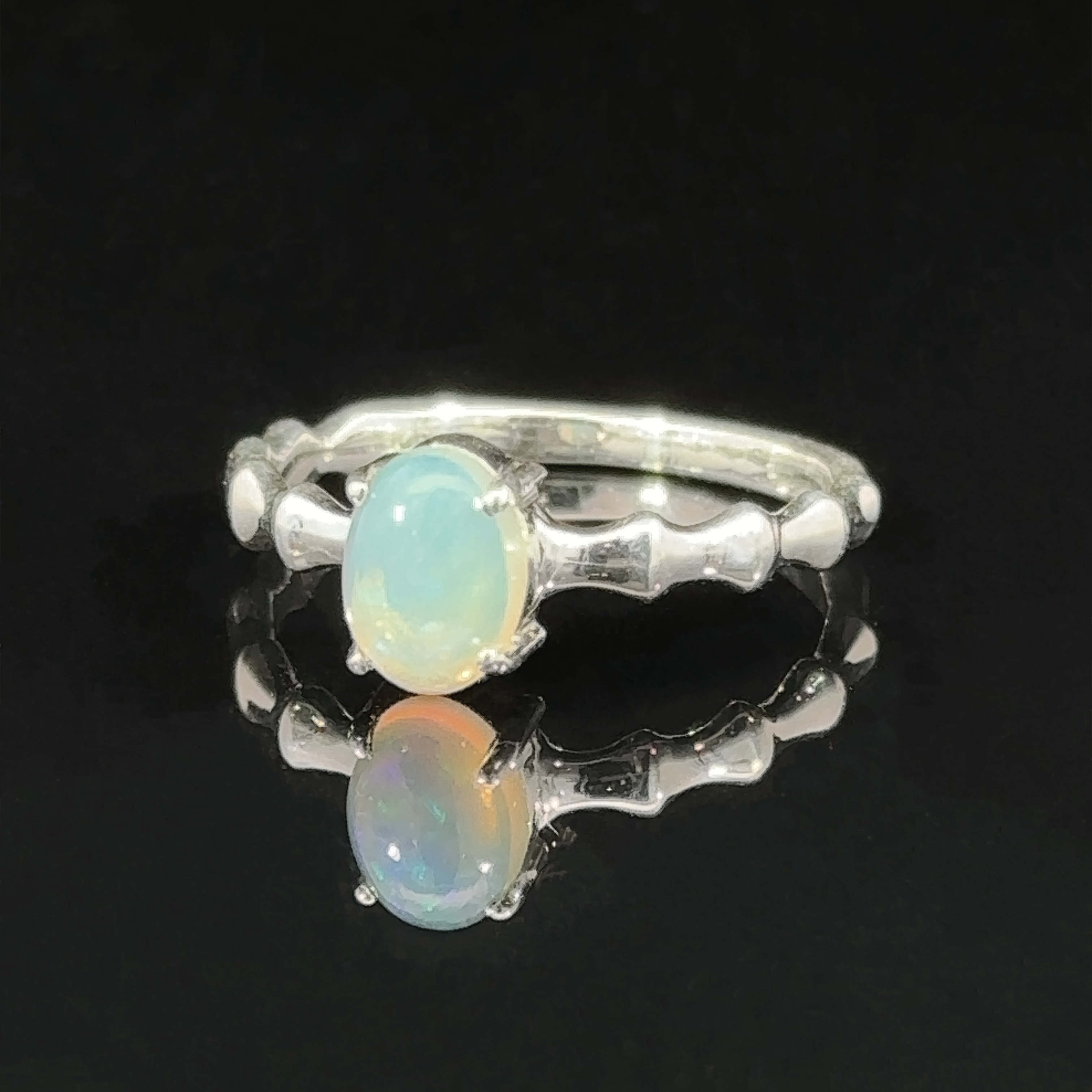 Pronged Oval Gemstone Ring with Textured Band with a blue topaz set on a reflective black surface.