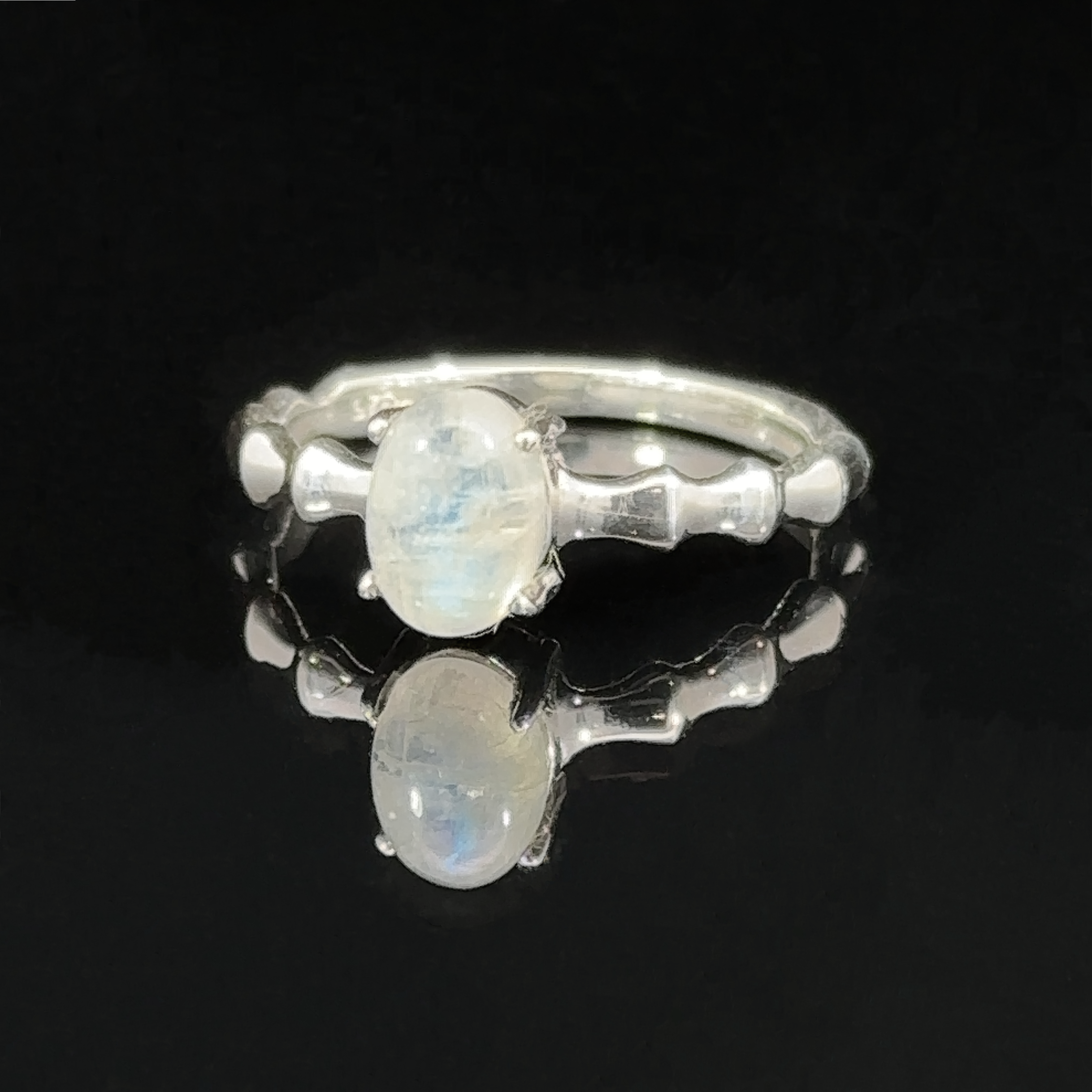 Pronged Oval Gemstone Ring with Textured Band with two sparkling gemstones on a reflective black surface.