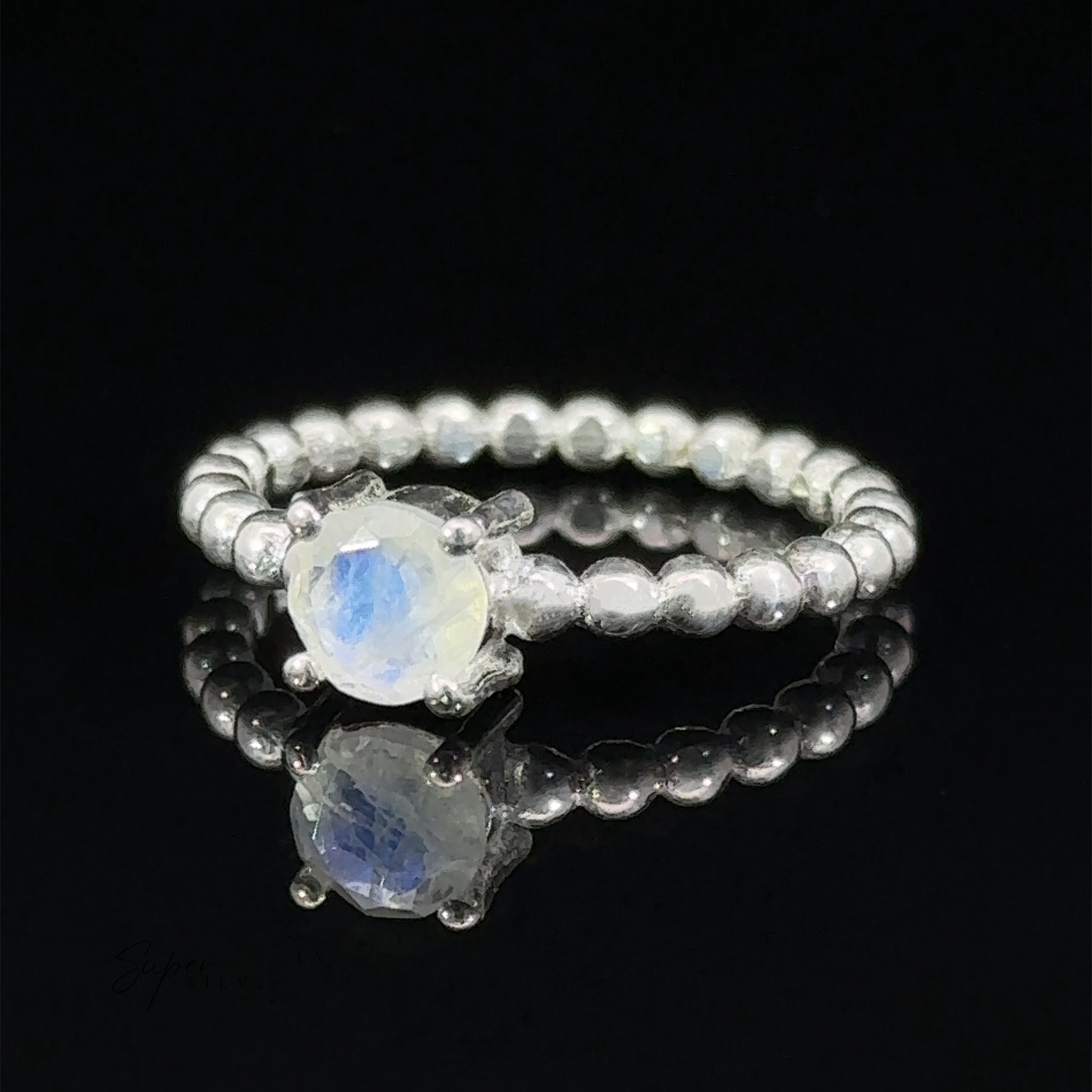 A Stunning Circular Gemstone Ring with a round-cut moonstone set on a beaded band, displayed on a reflective black surface.