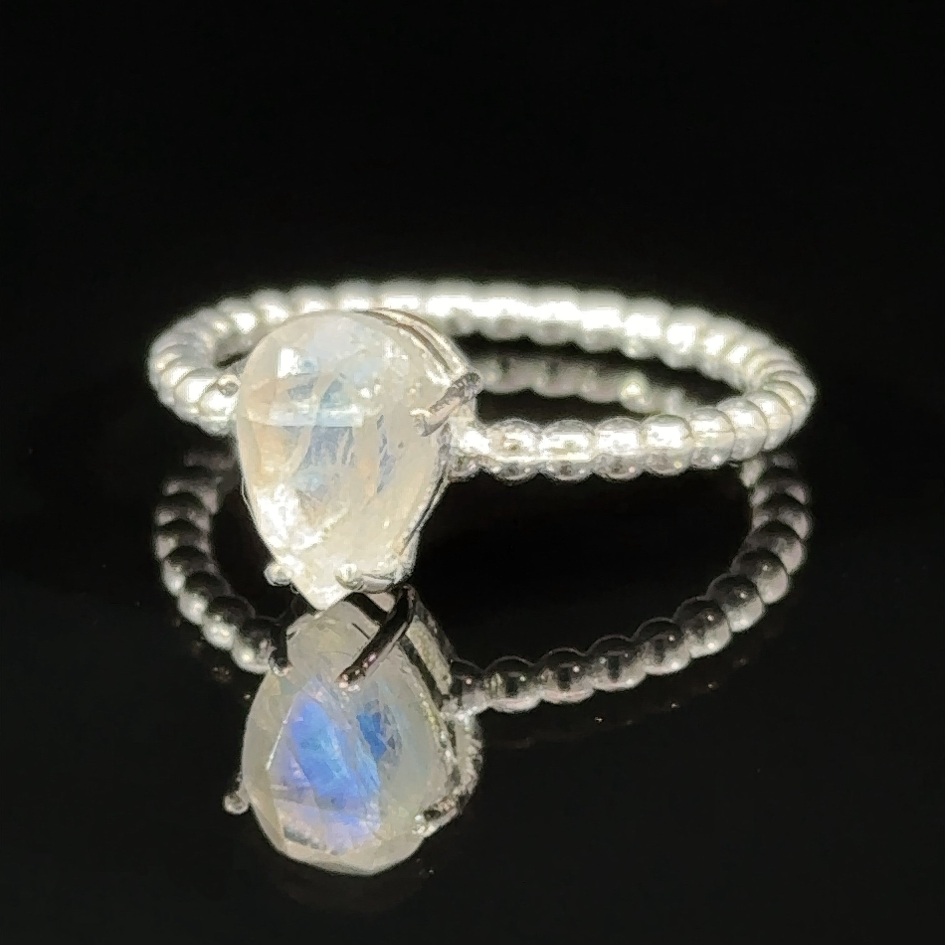 Vibrant Teardrop Gemstone Ring with Beaded Band with a pear-shaped opal set in a prong setting on a reflective surface against a black background.