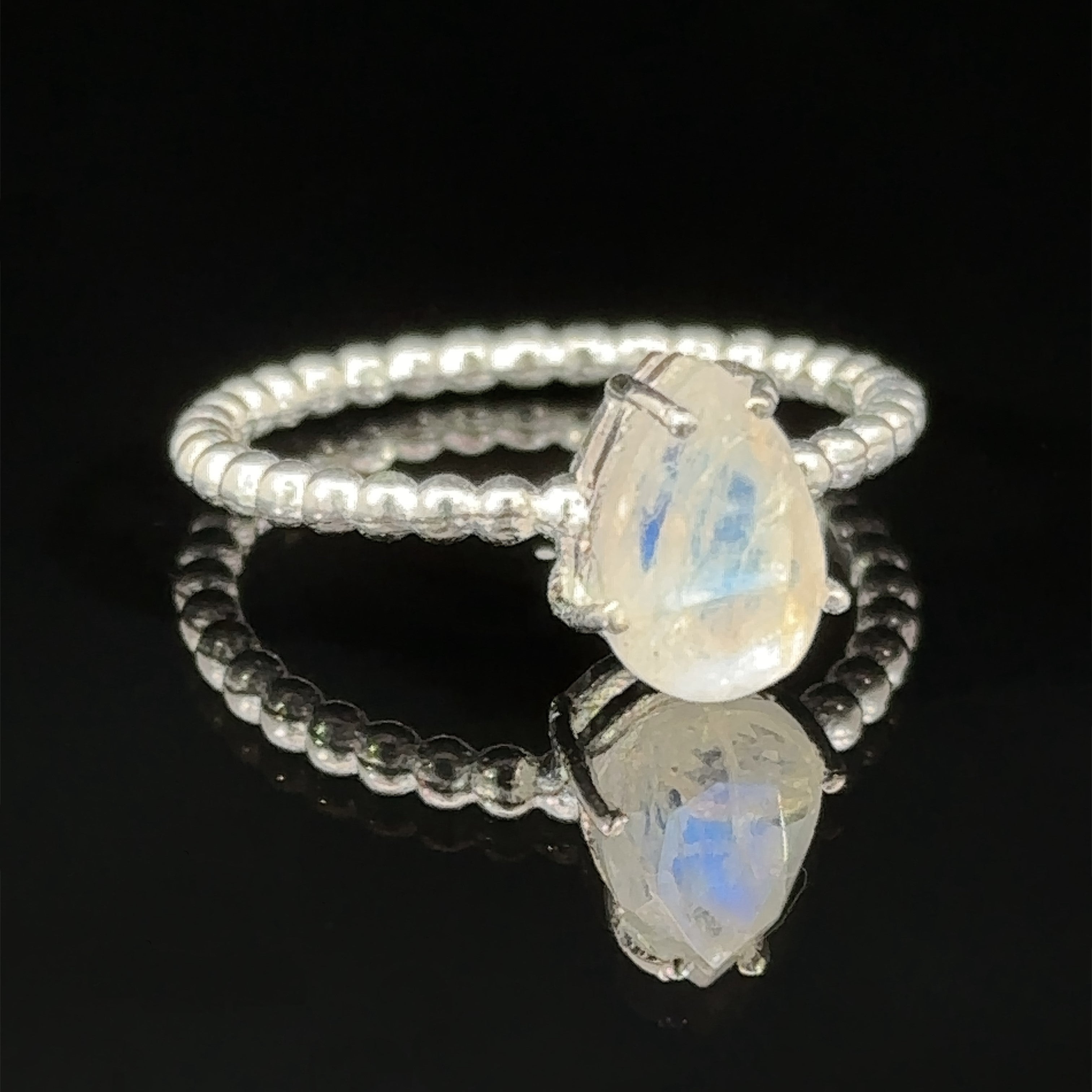 Vibrant Teardrop Gemstone Ring with Beaded Band with an oval opal stone, reflected on a glossy surface in a prong setting.