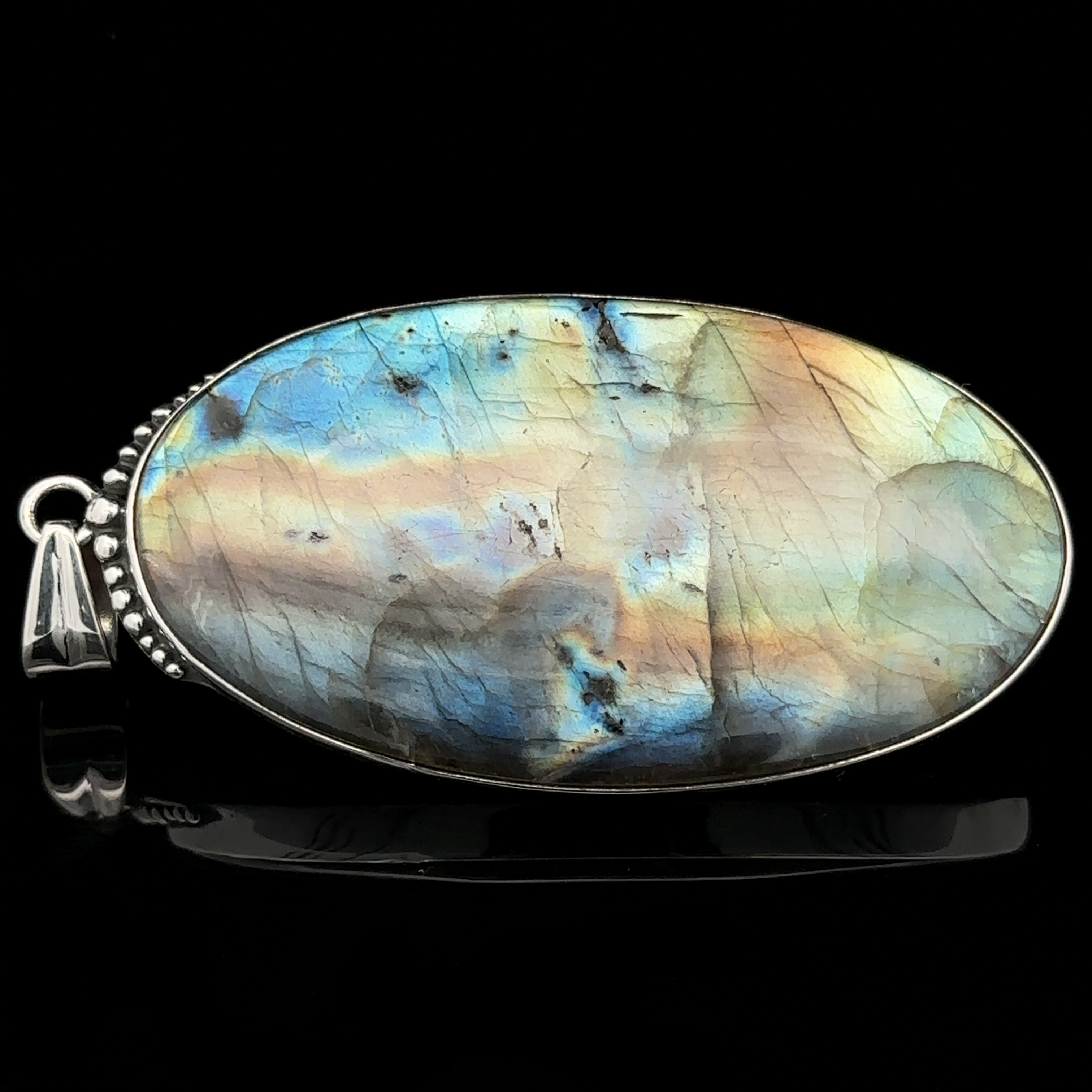 A polished, oval-shaped pendant featuring a labradorite gemstone with iridescent blue and brown hues, set in a sterling silver bezel against a black background. This statement piece is a stunning addition to any collection of XL Statement Oval Labradorite Pendants.