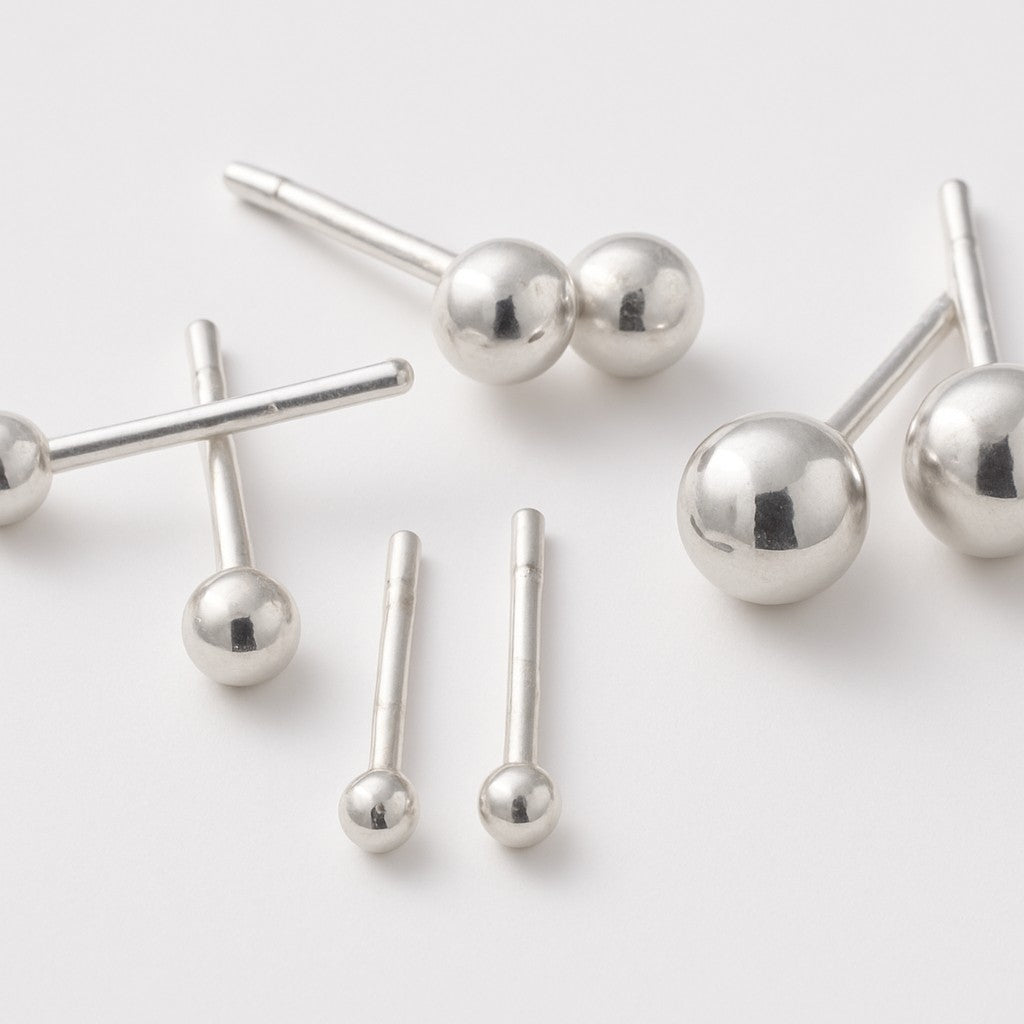 Simple Silver Ball Studs, inspired by molecular models and classic stud earrings, are arranged on a white surface—blending scientific inspiration with everyday essential style.