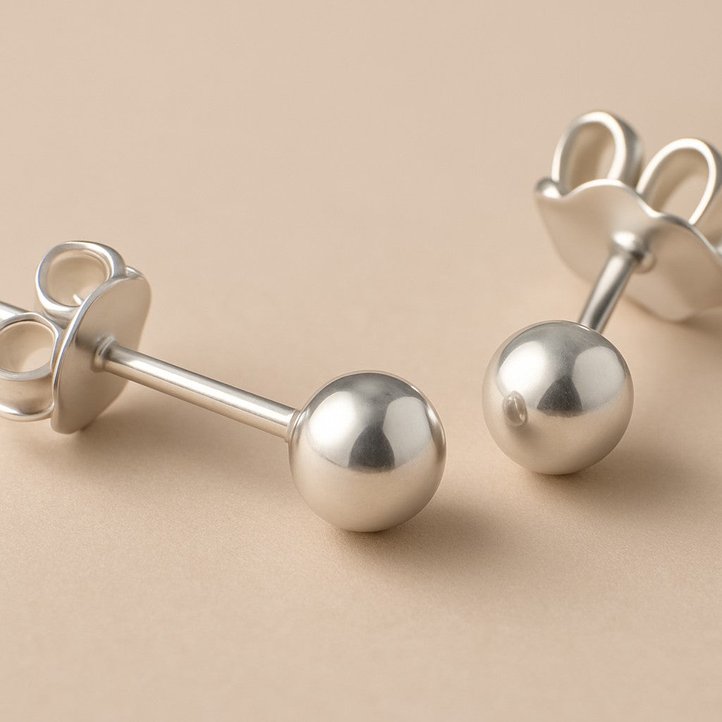 Simple Silver Ball Studs with butterfly backs rest on a beige surface—classic sterling silver earrings that are perfect for everyday wear.