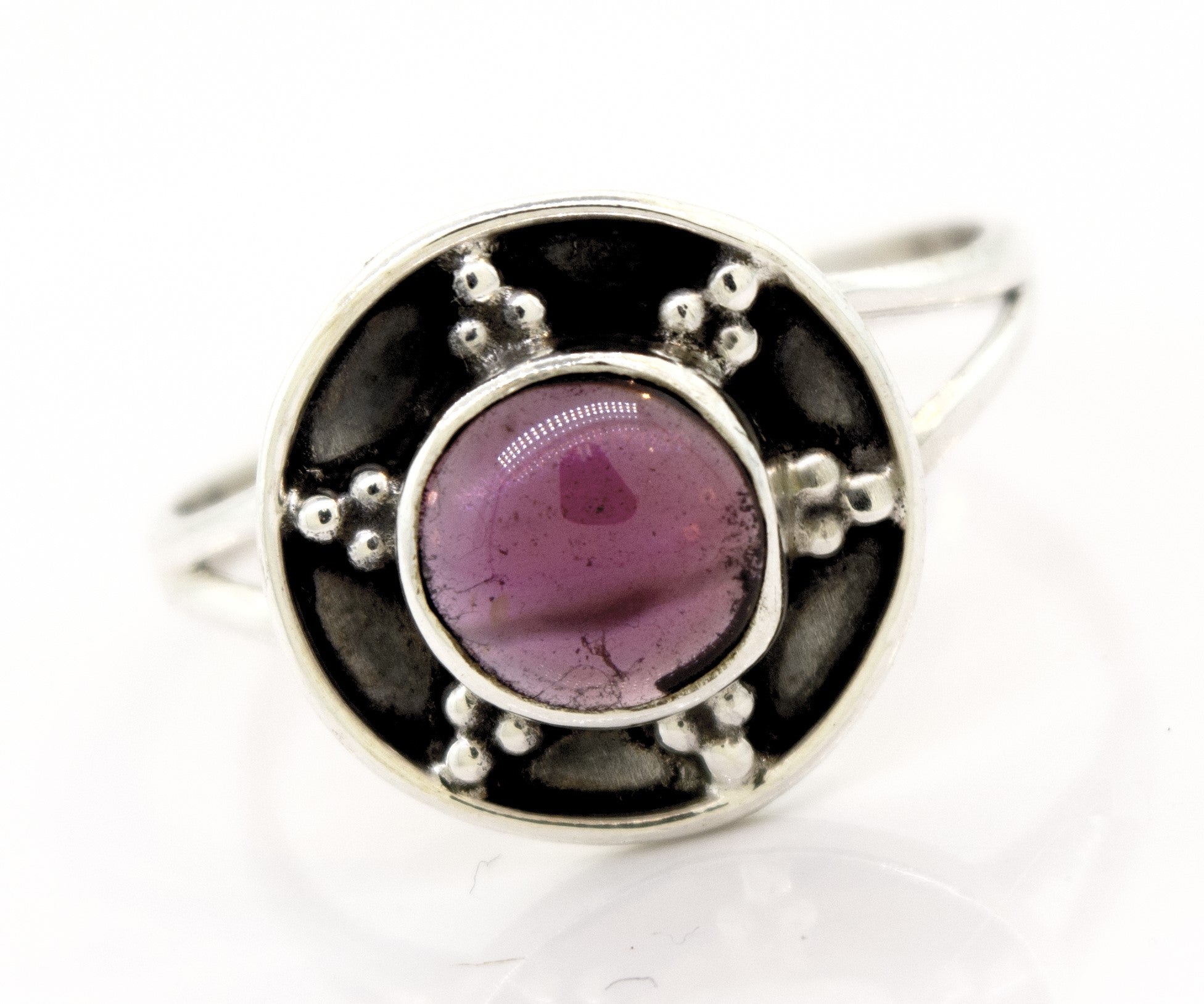 A Gemstone Ring With Unique Oxidized Design features a round purple gemstone set in a circular design with dotted metal embellishments, creating a stunning piece of gemstone jewelry.