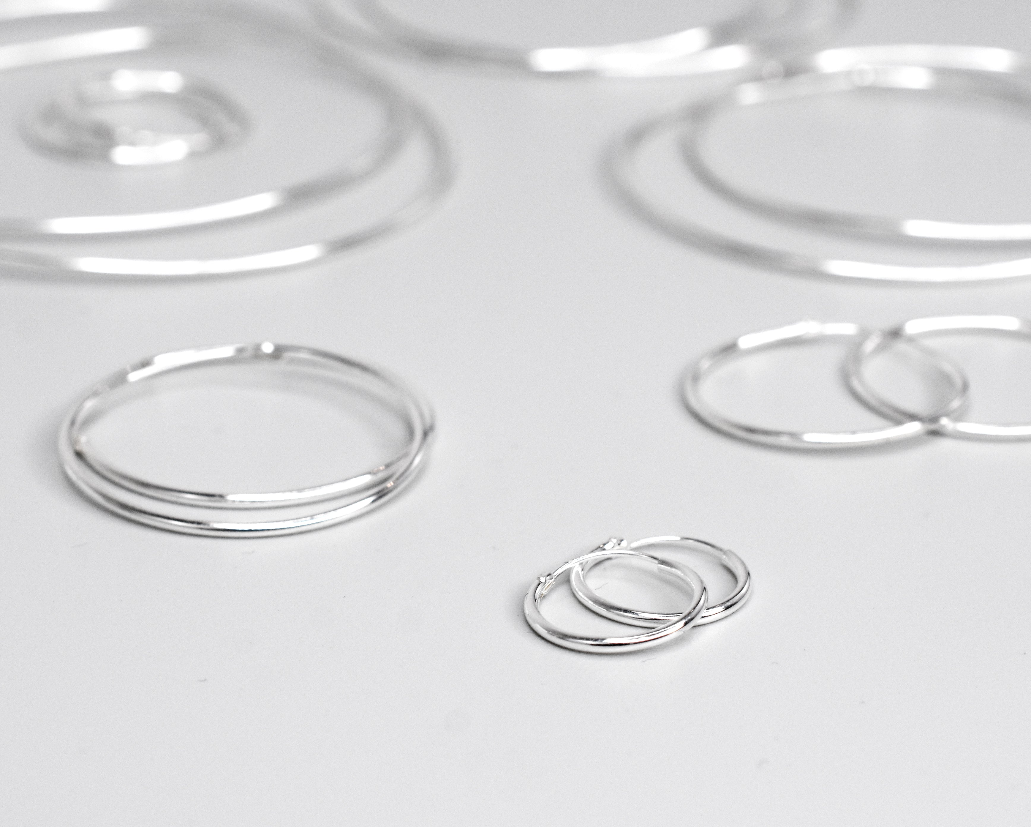 The 1.2mm Infinity Hoops, crafted from .925 Sterling Silver, are beautifully displayed on a white surface.