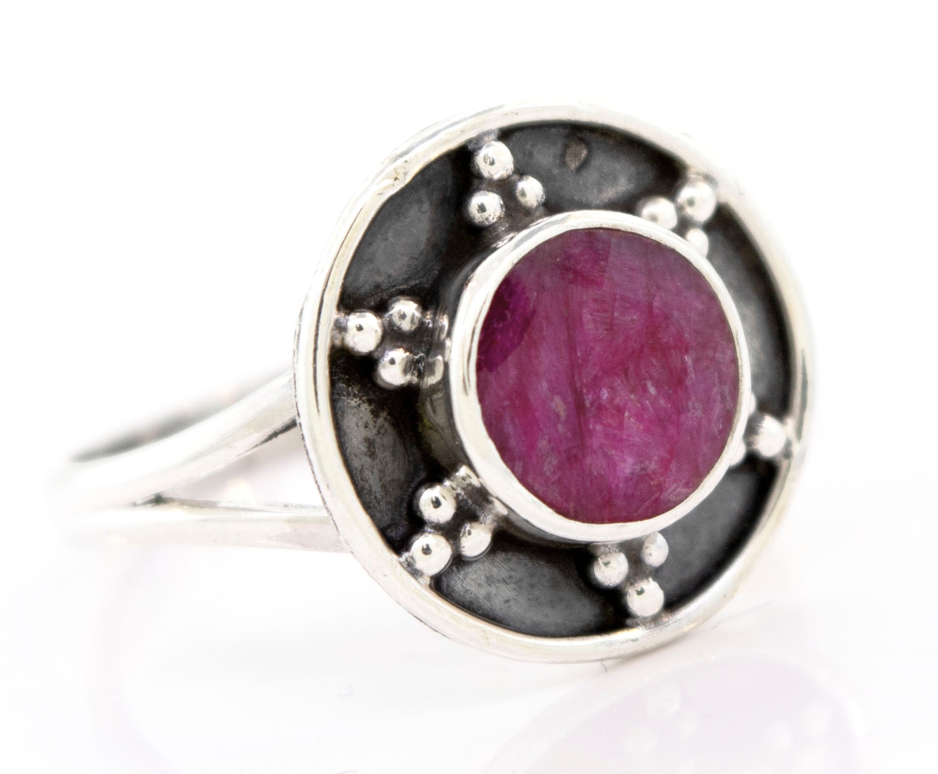 Close-up of a Gemstone Ring With Unique Oxidized Design with a round red gemstone set in the center, surrounded by a dark background and small metallic beads.