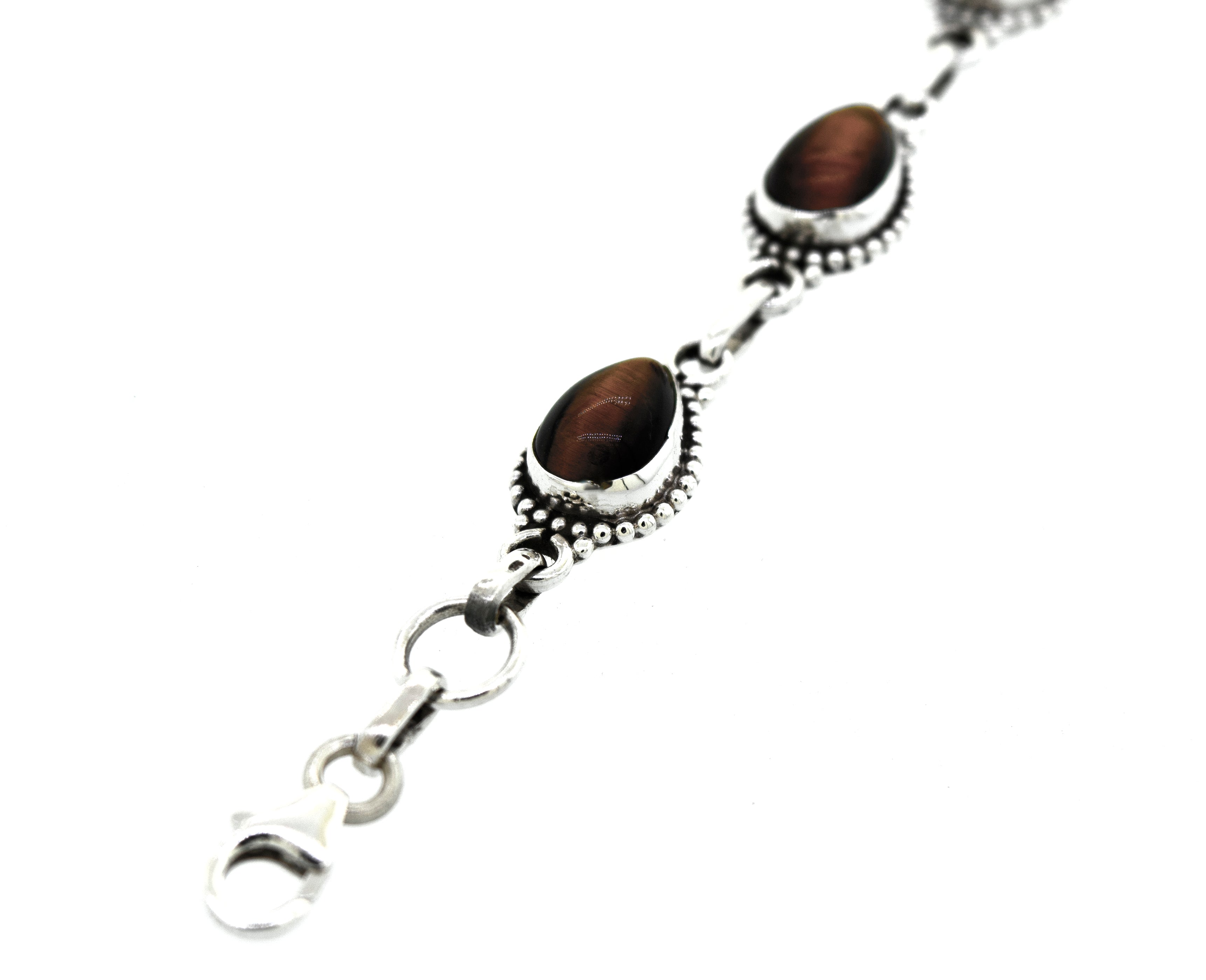 A Teardrop Shape Stone Bracelet With Ball Border with two oval-shaped, brown Tiger's Eye gemstones in decorative settings, connected by small links and a lobster clasp.