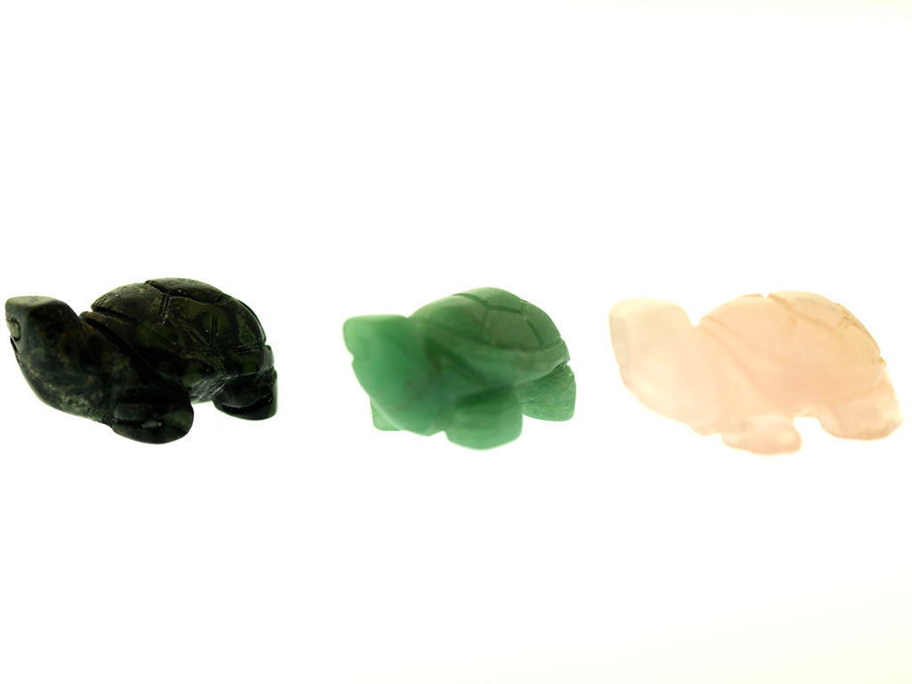 Three Carved Turtle Gemstone Figures made of different colored stones: dark green Aventurine, light green, and light pink Rose Quartz, on a white background.