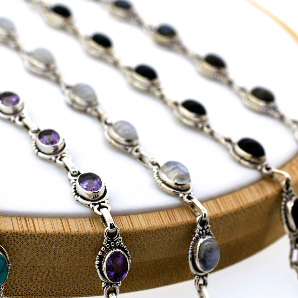 A group of oval gemstone bracelets with half ball border on a wooden stand by Super Silver.
