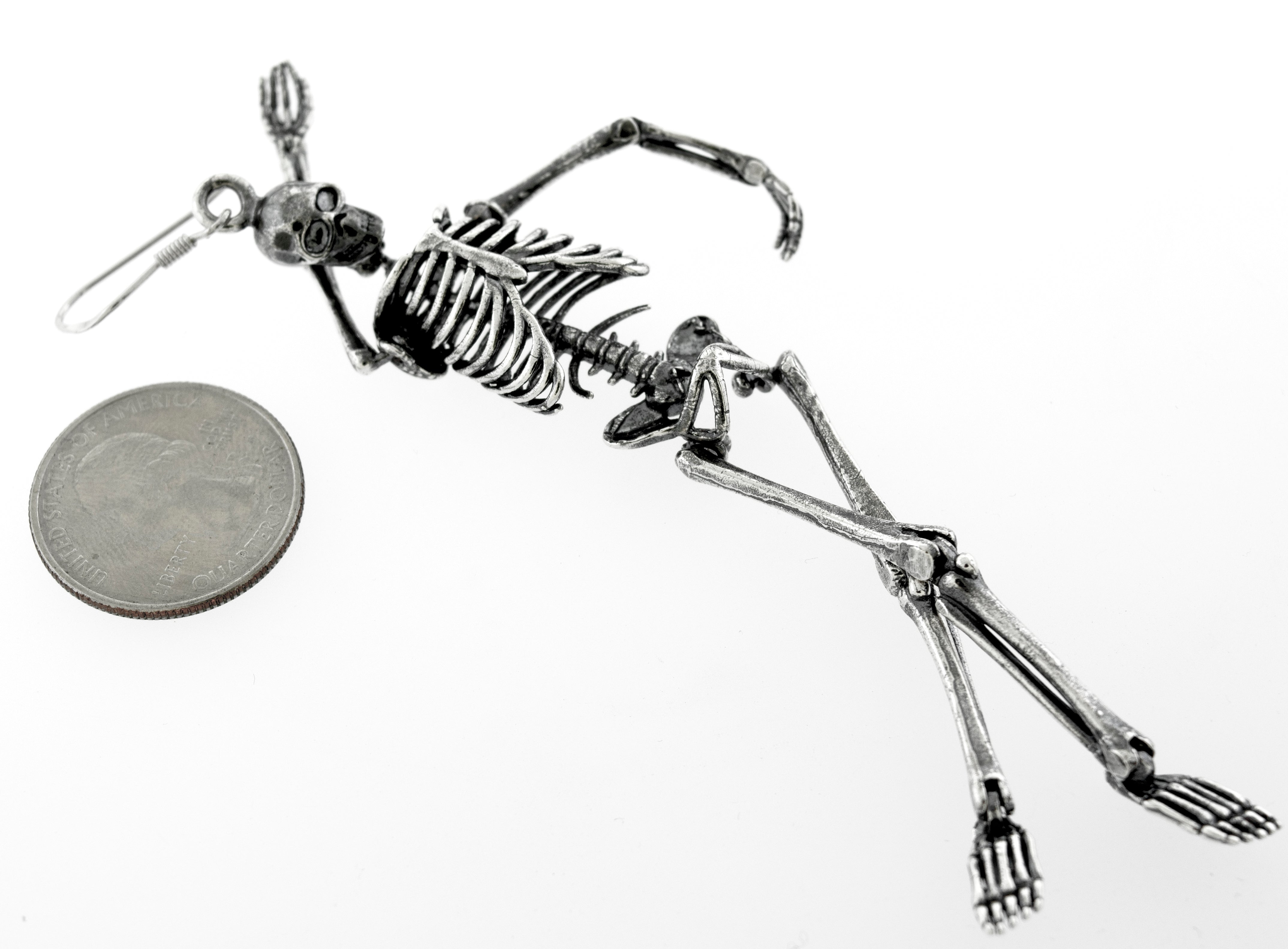 A spooky-themed Super Silver skeleton earring crafted in Sterling Silver, featuring a chilling design of a skeleton laying on top of a coin.