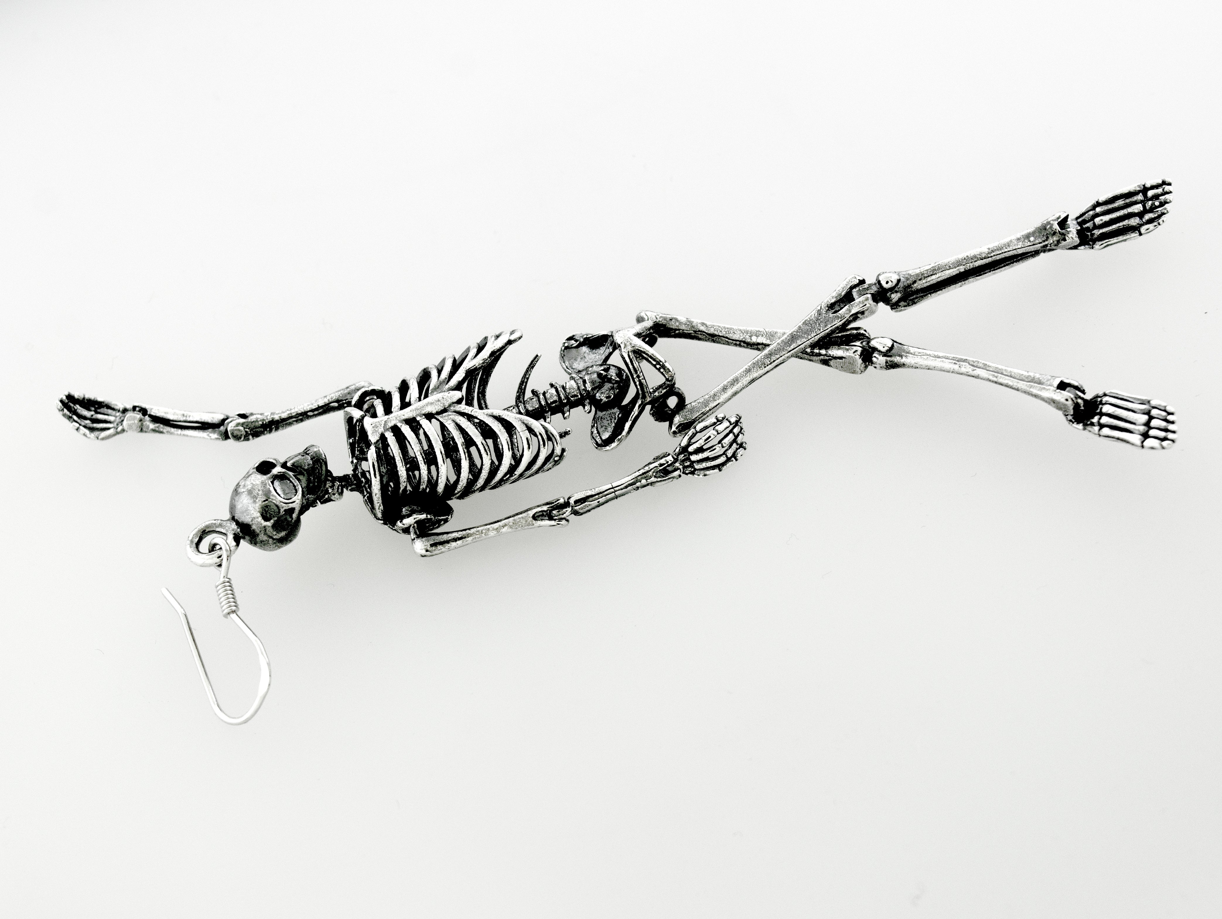 Spooky-themed Super Silver sterling silver skeleton earrings dangle from a chain on a white surface.