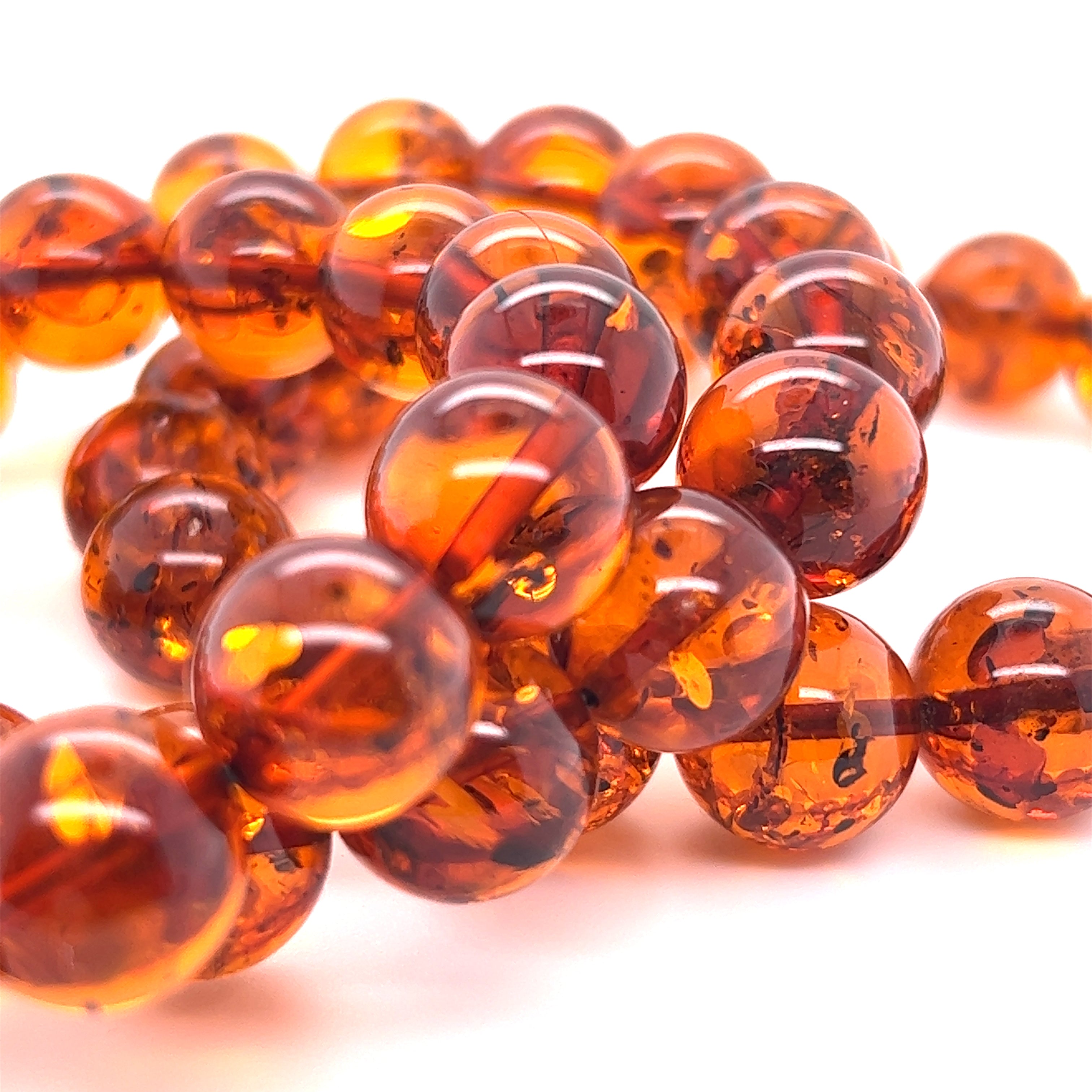 Close-up of the Captivating Classic Amber Bead Bracelet, showcasing polished cognac amber beads with their translucent orange and brown hues against a white background.