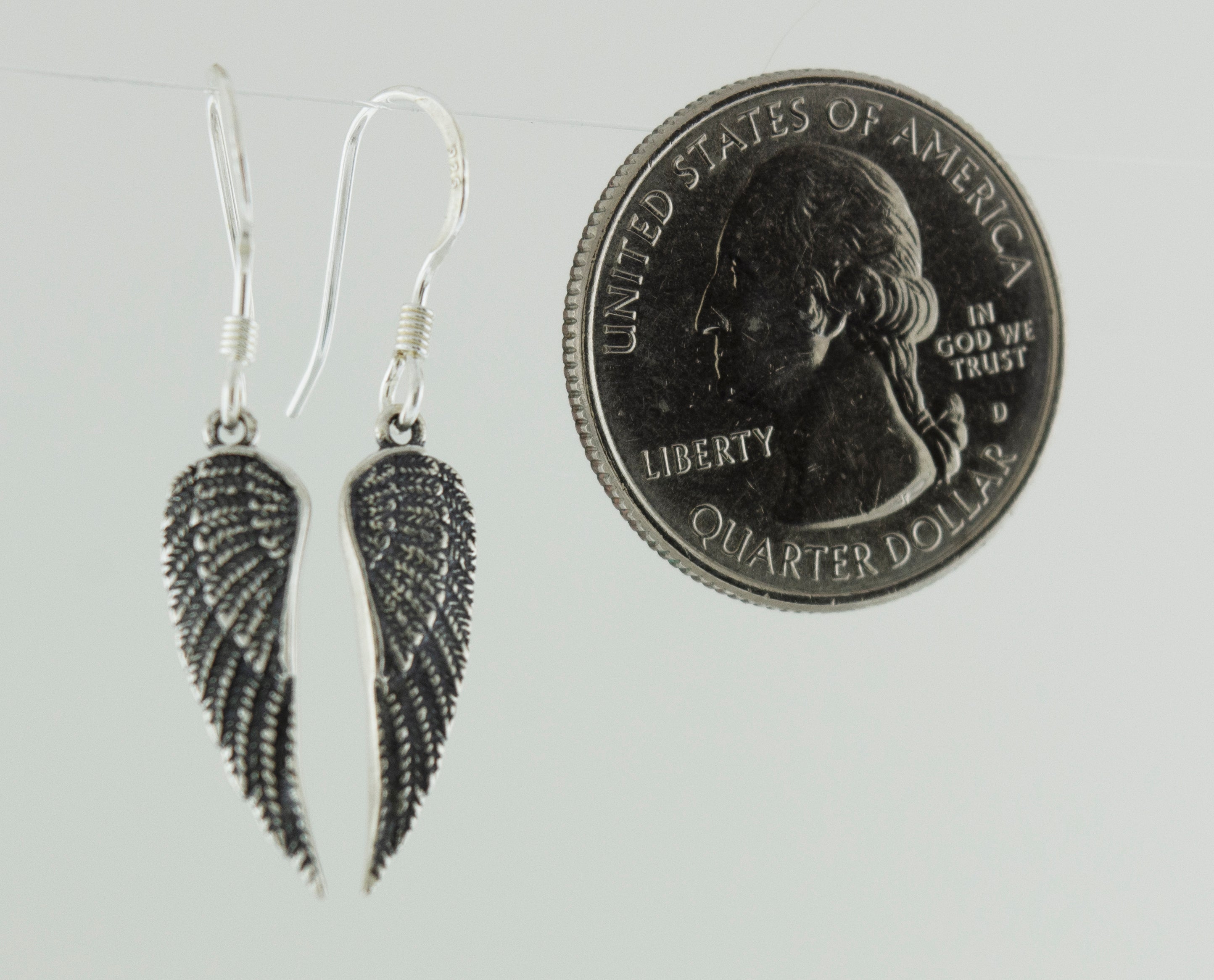 A pair of oxidized, .925 sterling silver Dainty Wing Earrings by Super Silver next to a penny.