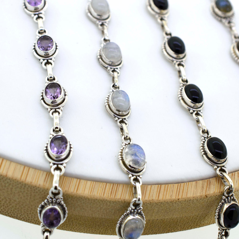 A chic display of Super Silver's Oval Gemstone Bracelets With Half Ball Border on a bohemian wooden stand.