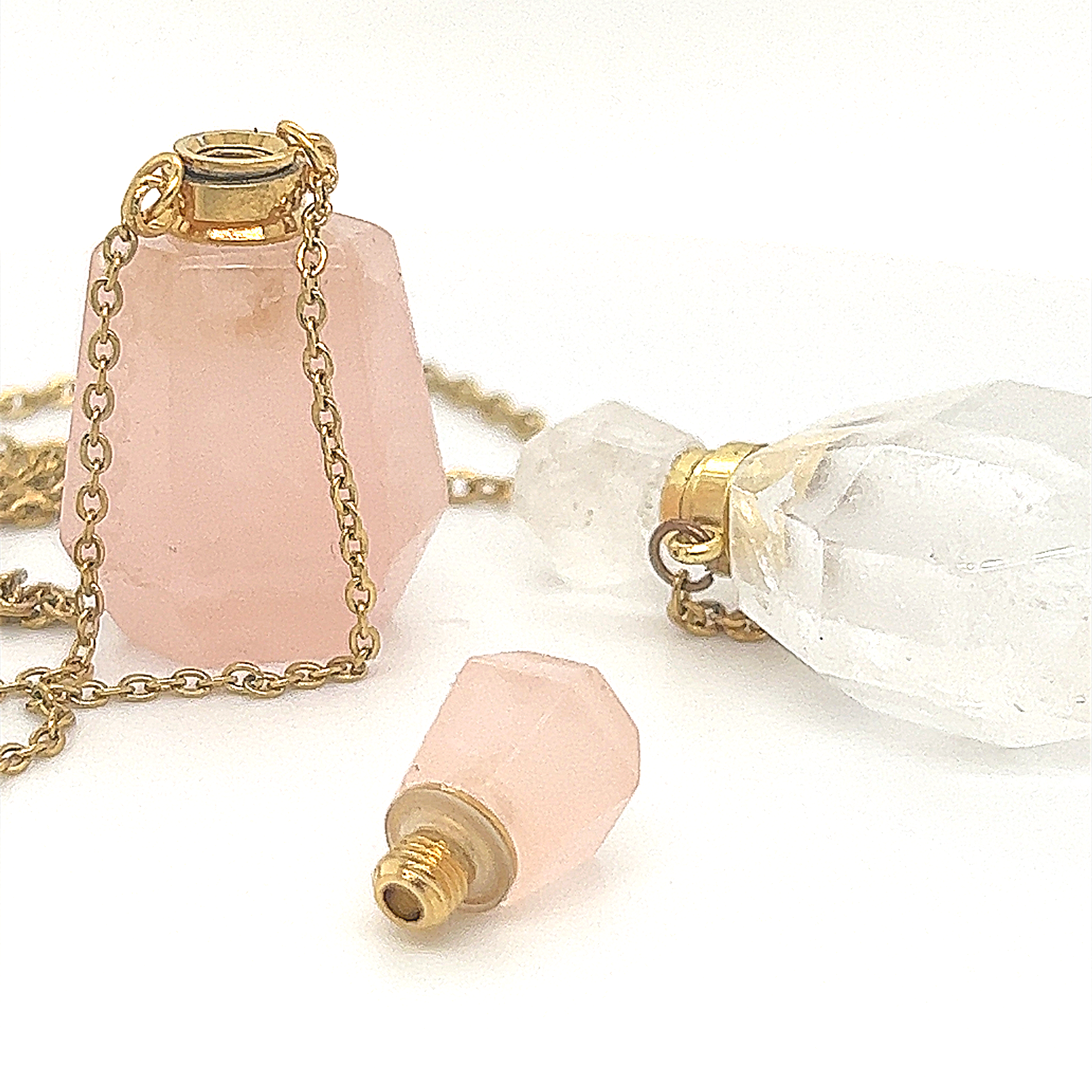 A pink glass bottle with a gold chain, ideal for storing essential oils or as a Crystal Perfume Vial Necklace featuring a quartz stone by Super Silver.