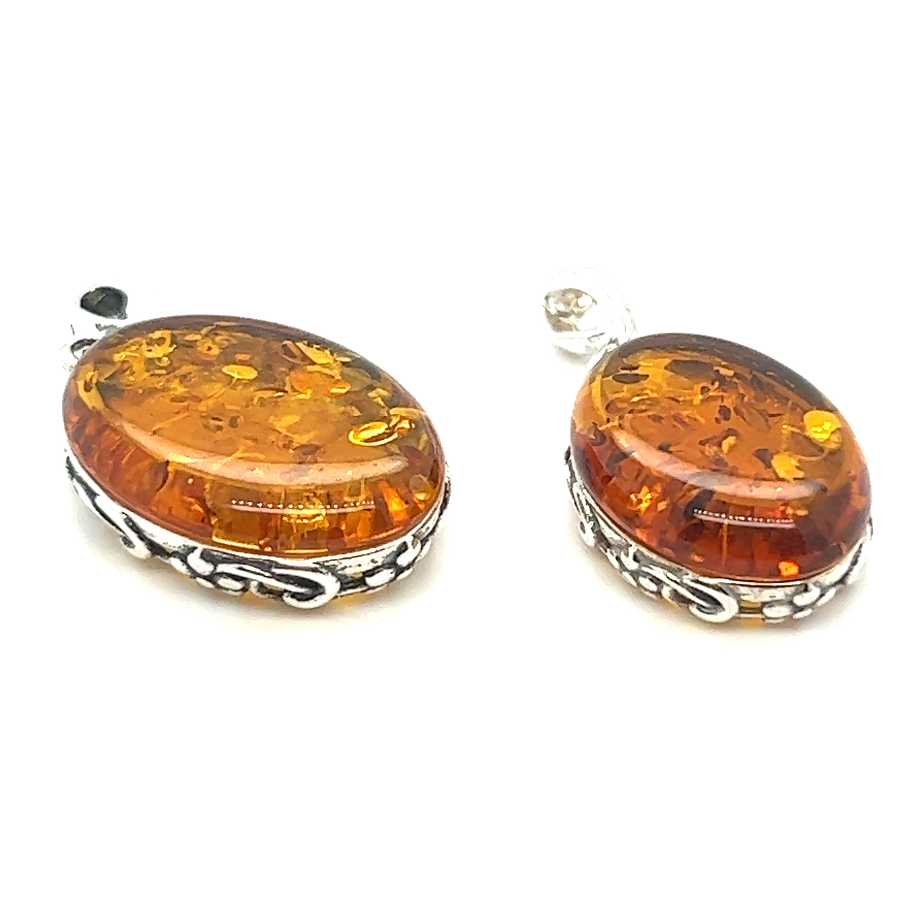 Two Super Silver cognac amber oval pendants with floral border on a white background. One pendant features the Cognac Amber Oval Pendant with Floral Border, showcasing a vintage-styled design.