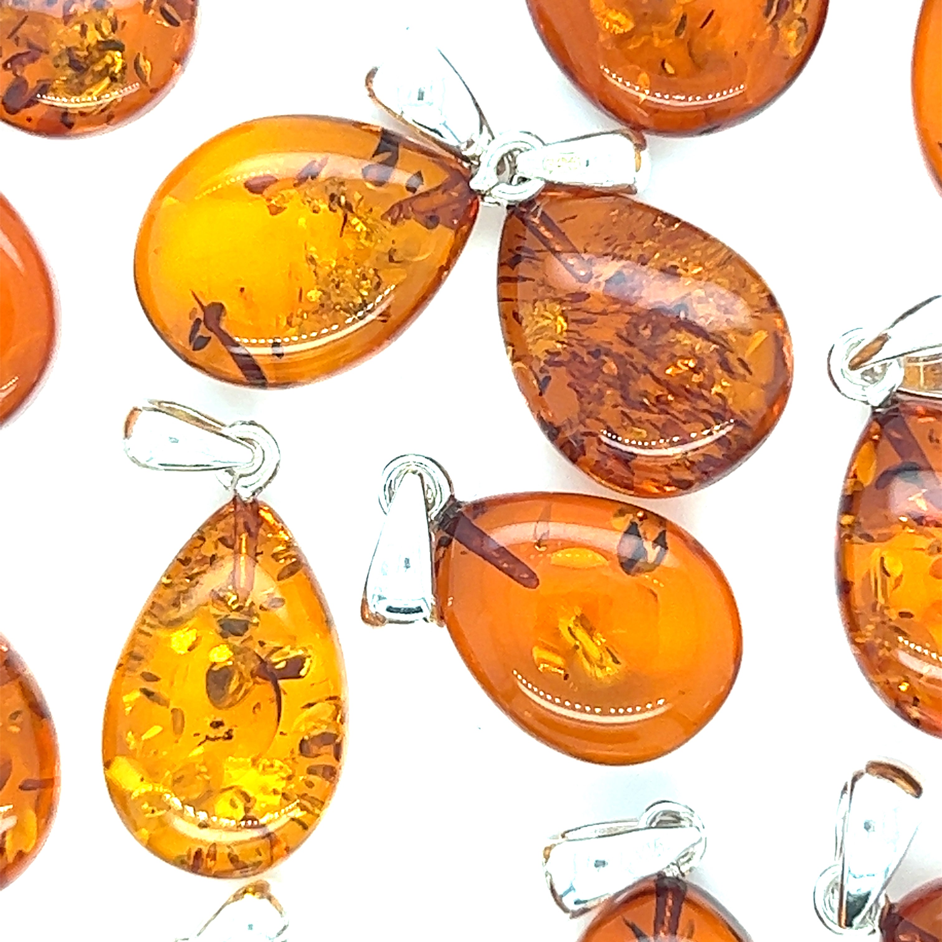 A collection of Super Silver Teardrop Amber Pendants emitting healing energy, showcased on a pristine white background.