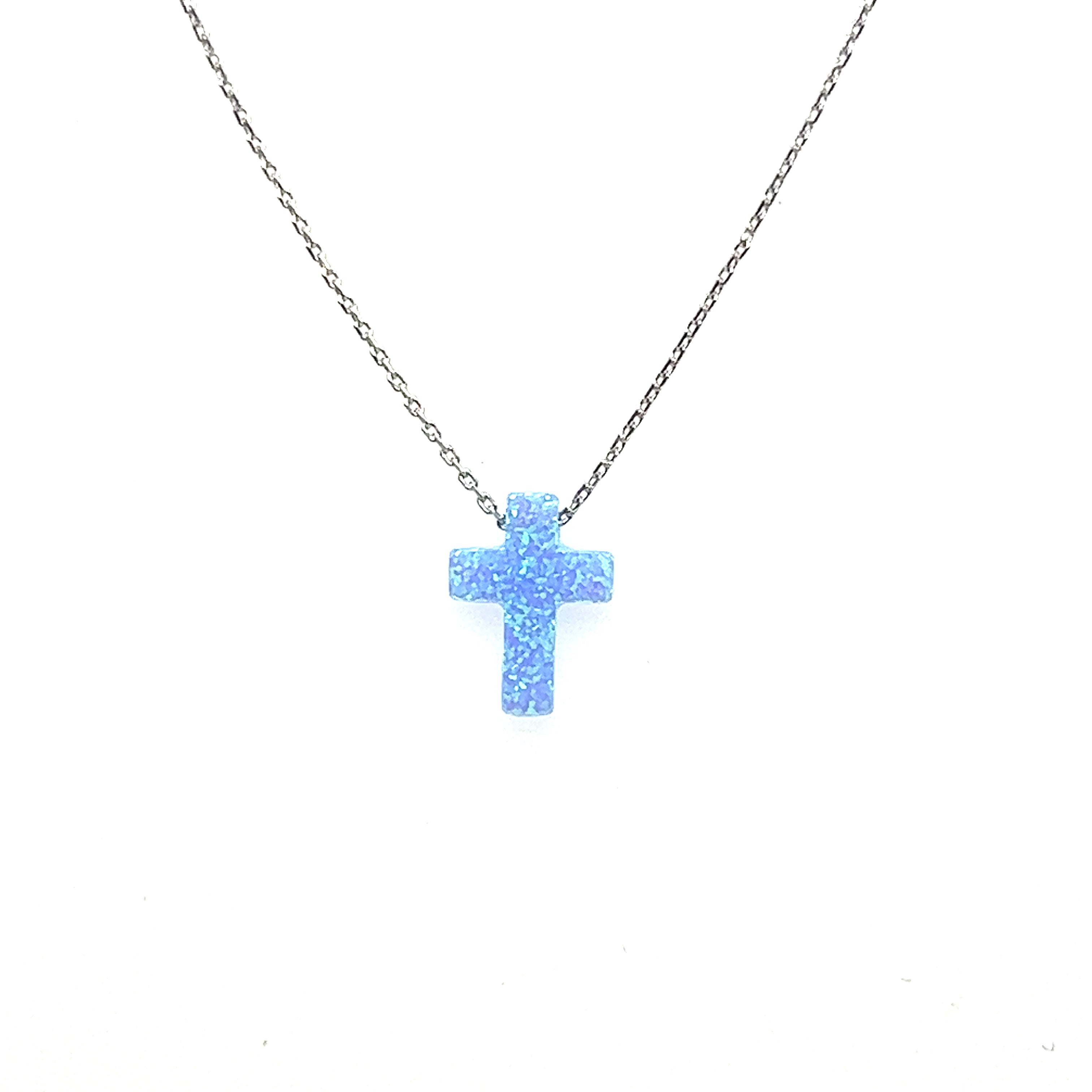 A delicate Blue Opal Cross Necklace, adorned with a calming ocean blue stone and a sprinkle of glitter, hangs gracefully from a Super Silver chain.