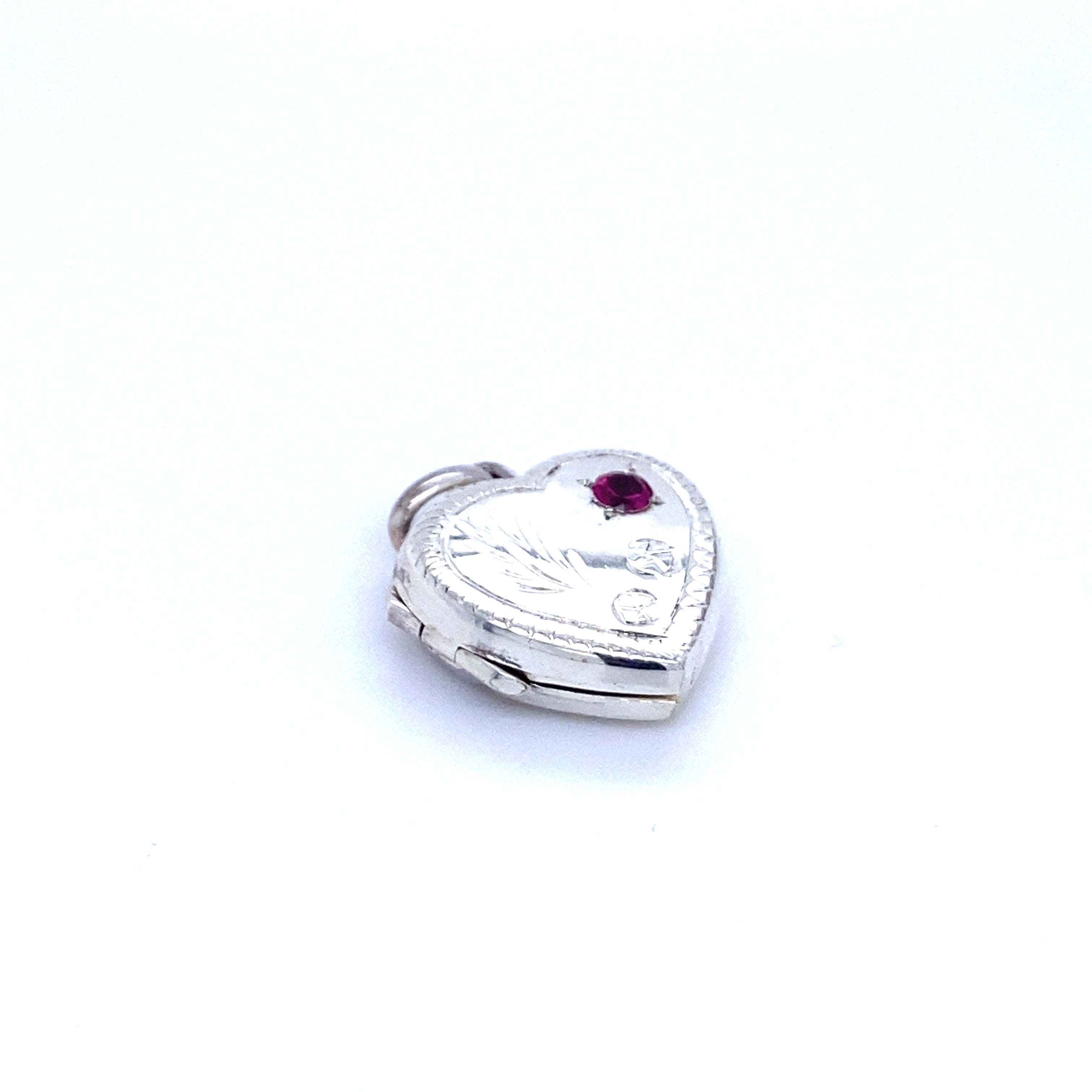 A Super Silver heart-shaped locket with a ruby stone and lacy etching, exuding romantic charm.