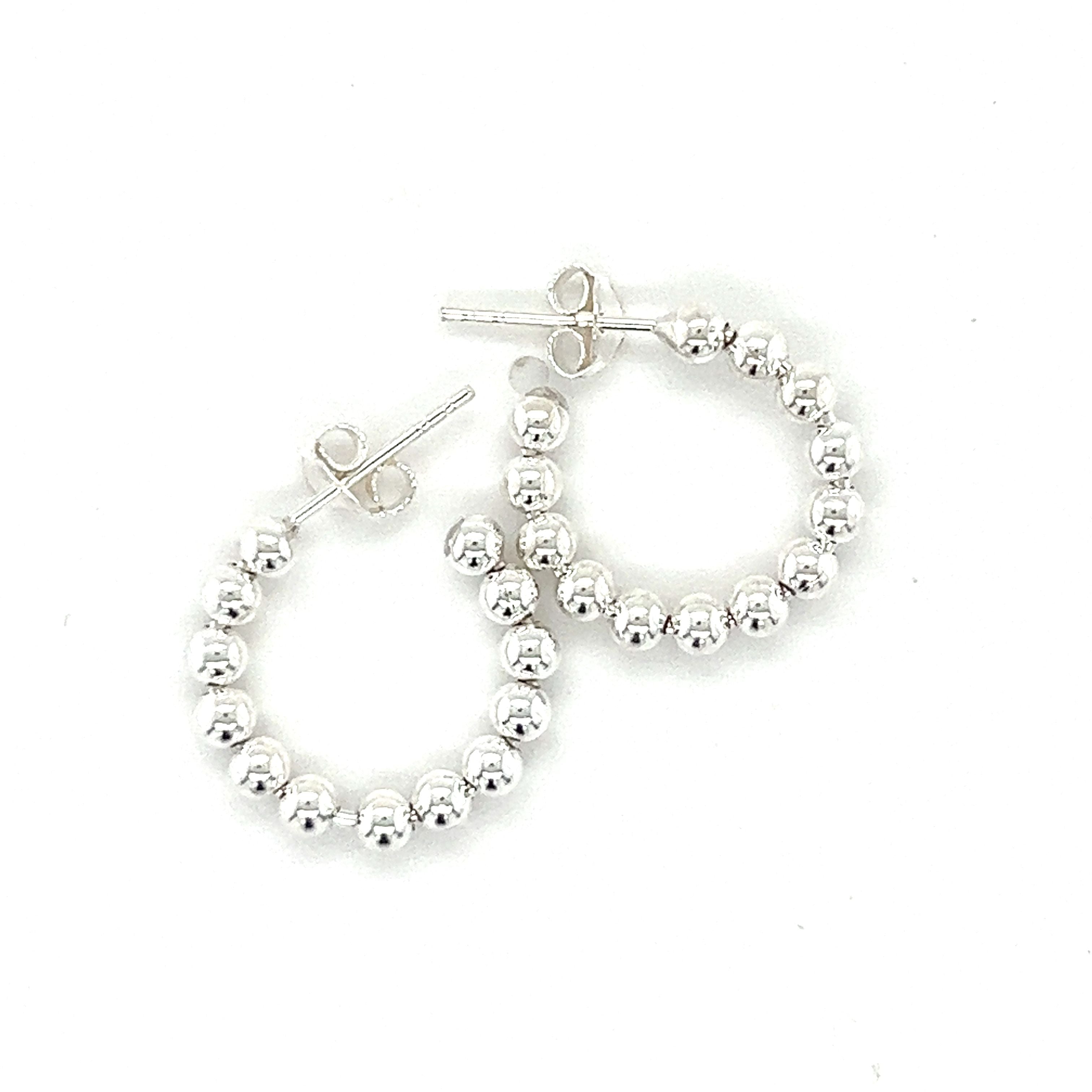 A pair of Delicate Ball Hoops With Post by Super Silver on a white background.