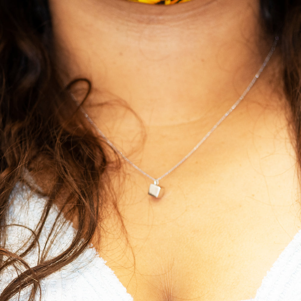 A woman wearing a Sleek Three Dimensional Silver Cube Necklace by Super Silver, with a flower on it.