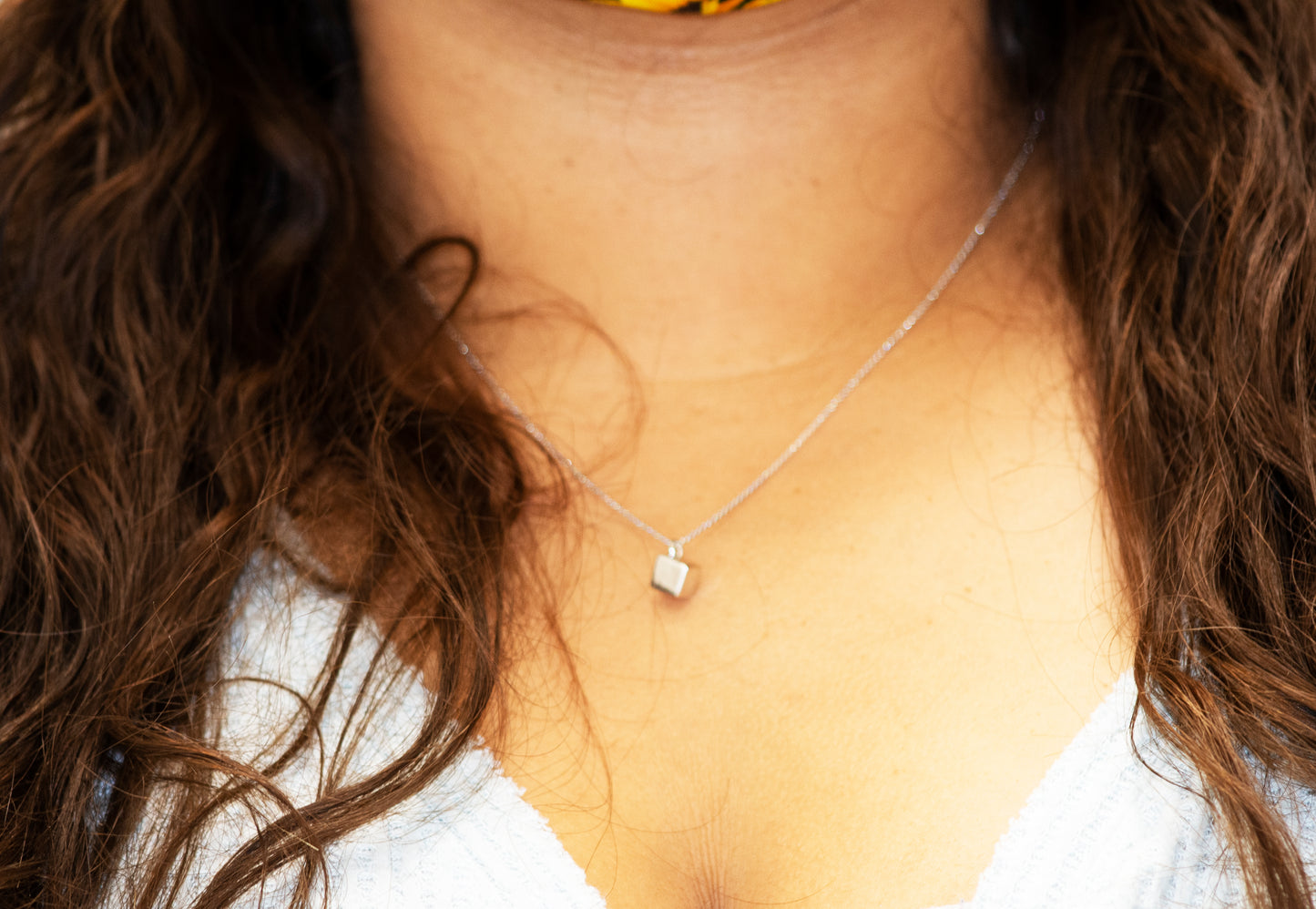 A woman wearing a Sleek Three Dimensional Silver Cube Necklace by Super Silver, with a flower on it.