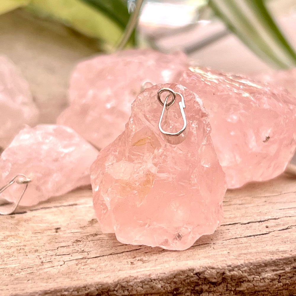 A bunch of pink Super Silver Raw Crystal Pendants on a wooden table.