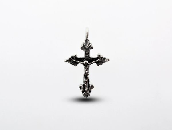 An ornate vintage Crucifix Charm with intricate details gleams against a plain white background.