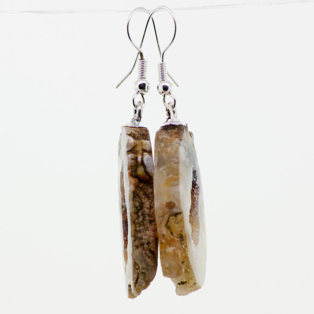 A pair of Super Silver Agate Geode Slice Earrings hanging from silver-plated hooks.