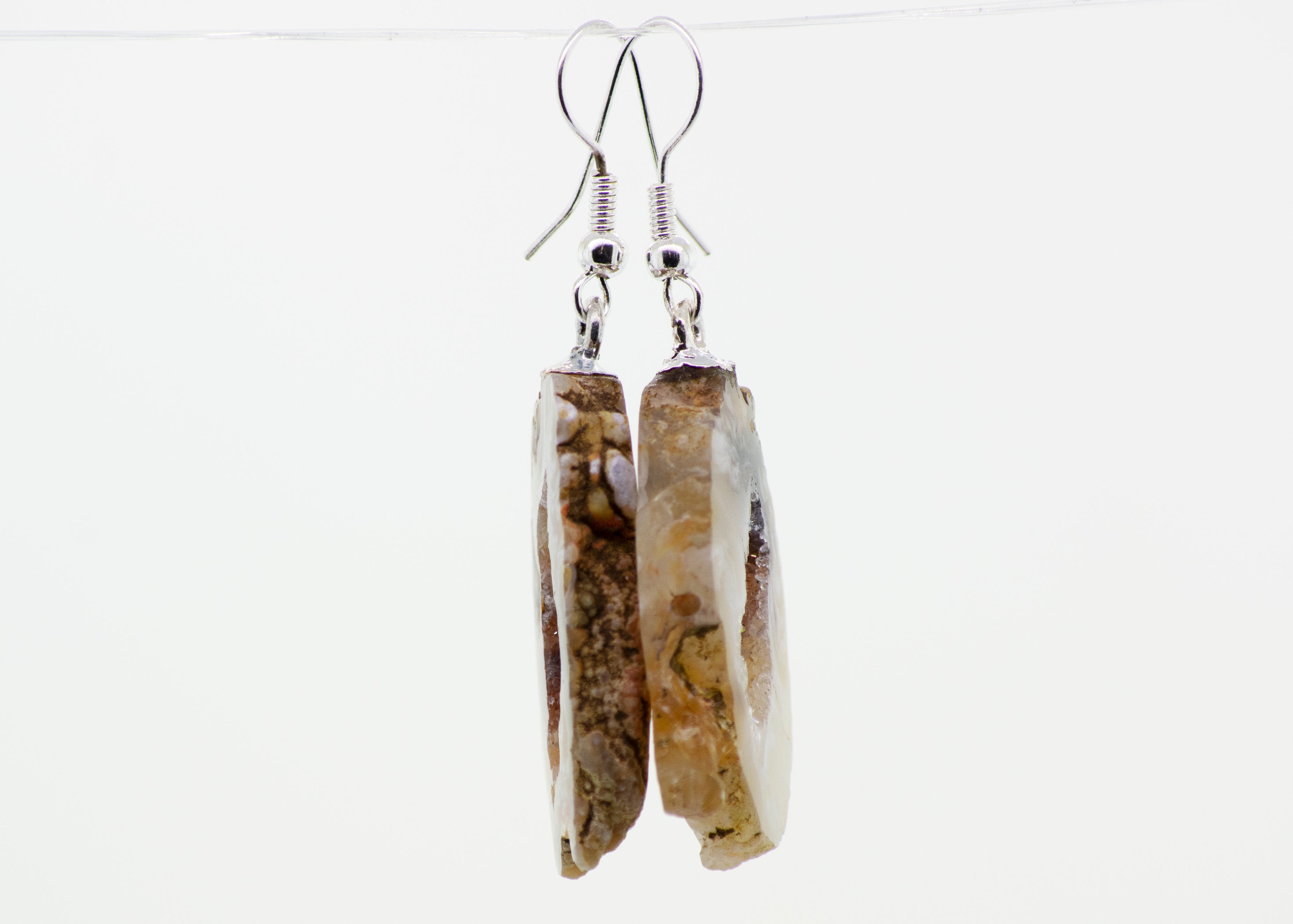 A pair of Super Silver Agate Geode Slice Earrings hanging from silver-plated hooks.