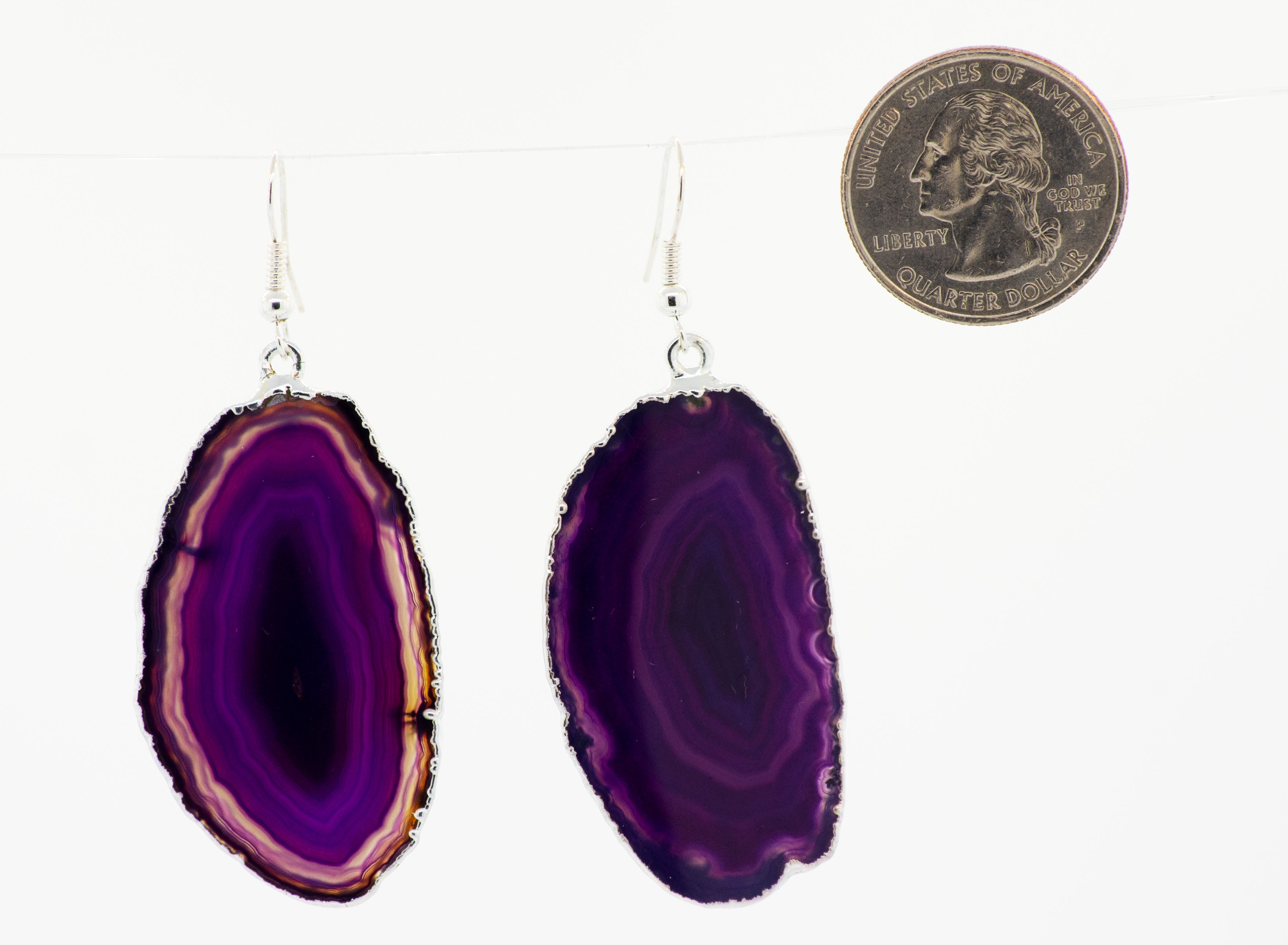 A purple slice of Super Silver dyed agate slice earrings, bordered by a silver-plated border, hanging from a string.