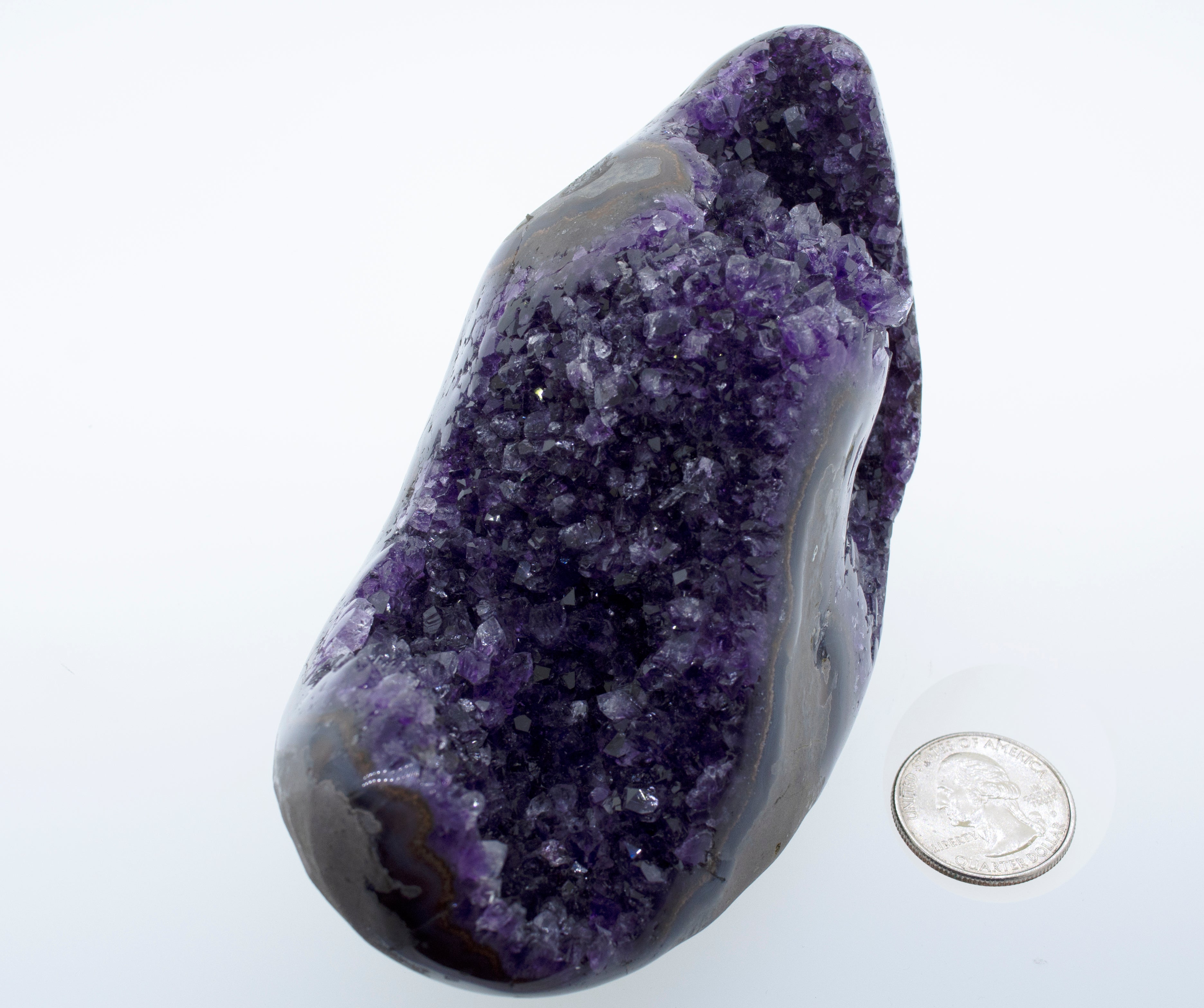 An Egg Shaped Amethyst Geode with a purple amethyst rock next to a dime.
