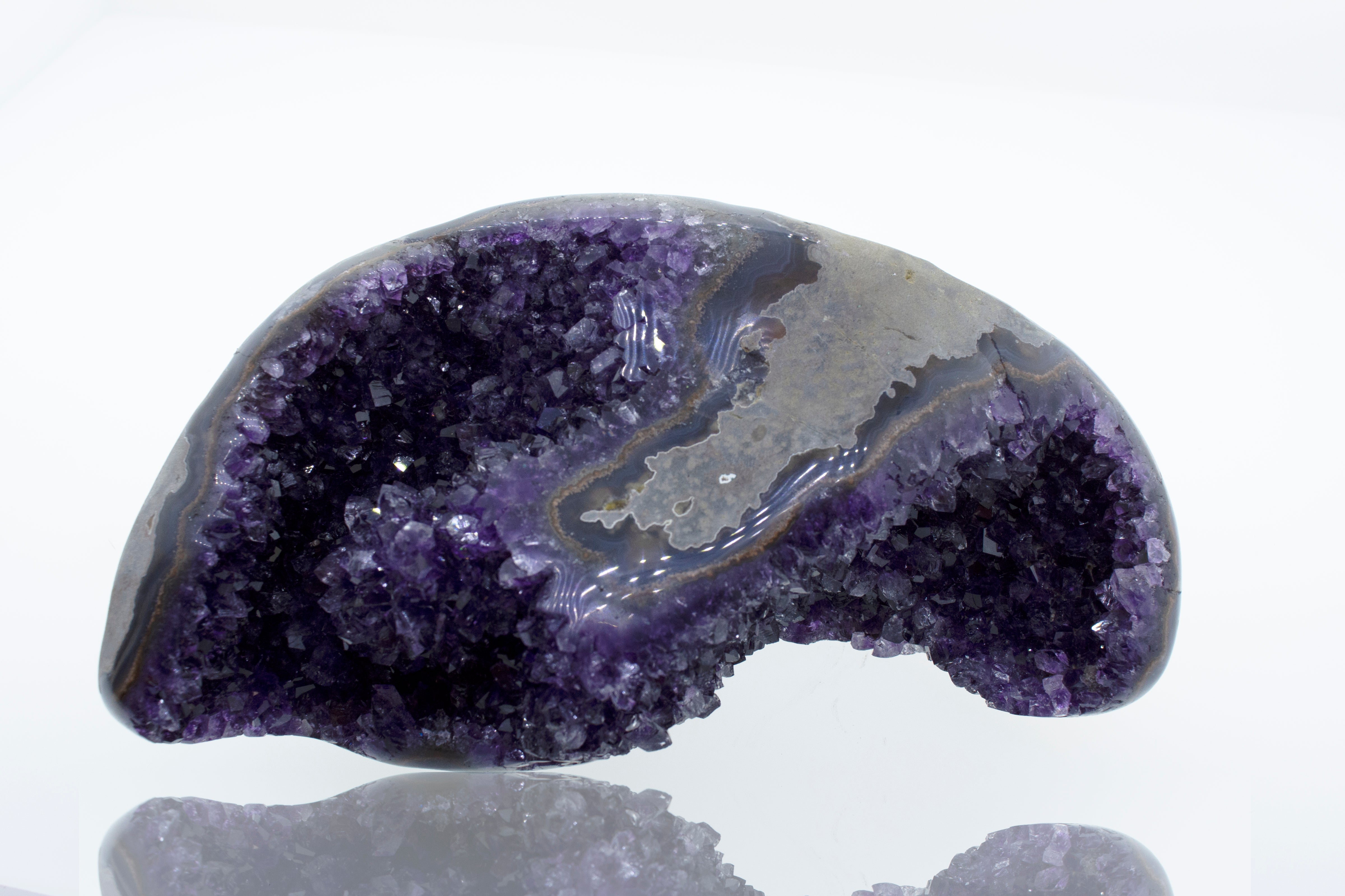 An Egg Shaped Amethyst Geode on a white surface.