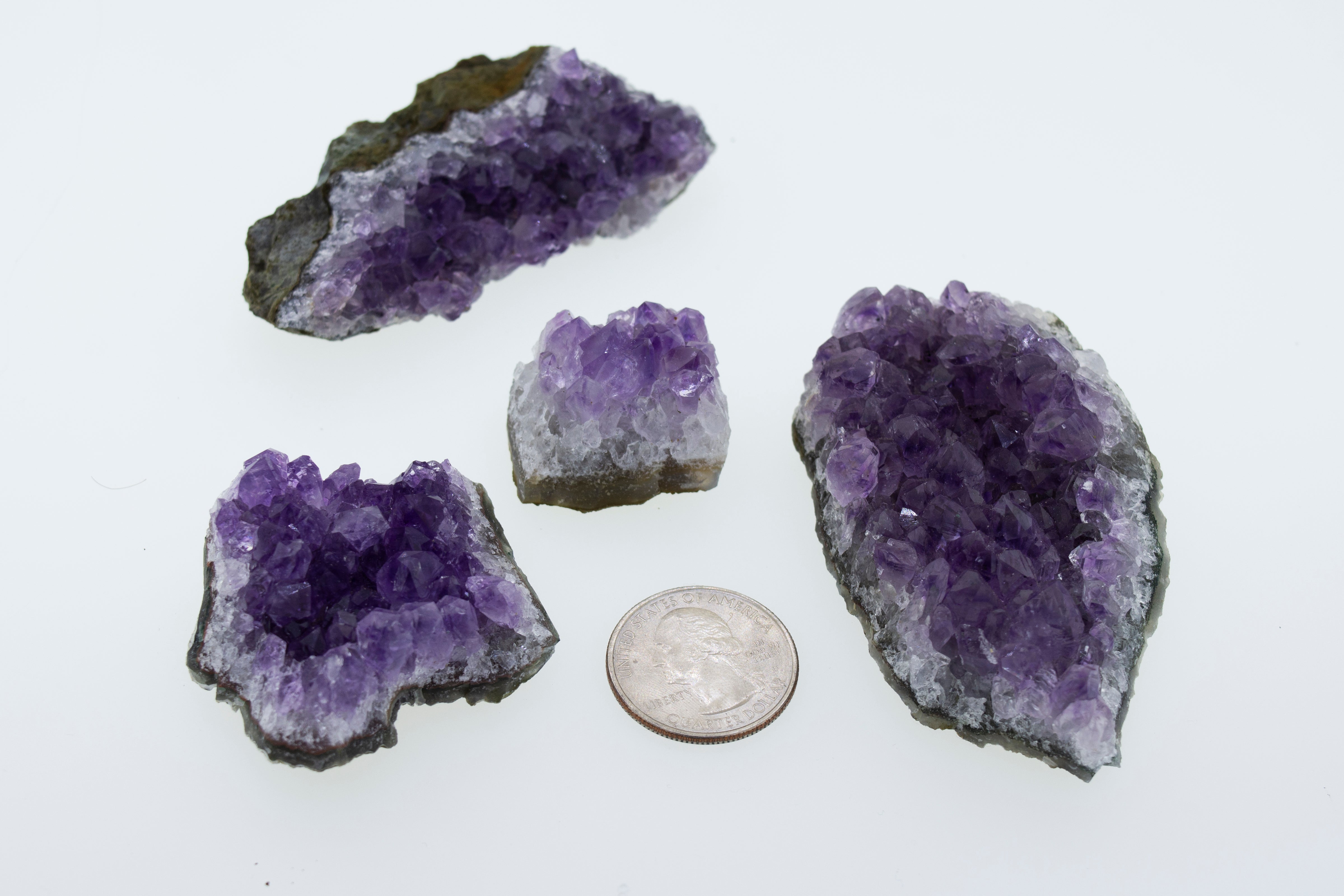 Four purple Amethyst Geodes in Varying Sizes next to a dime, perfect for boho decor or geode enthusiasts.