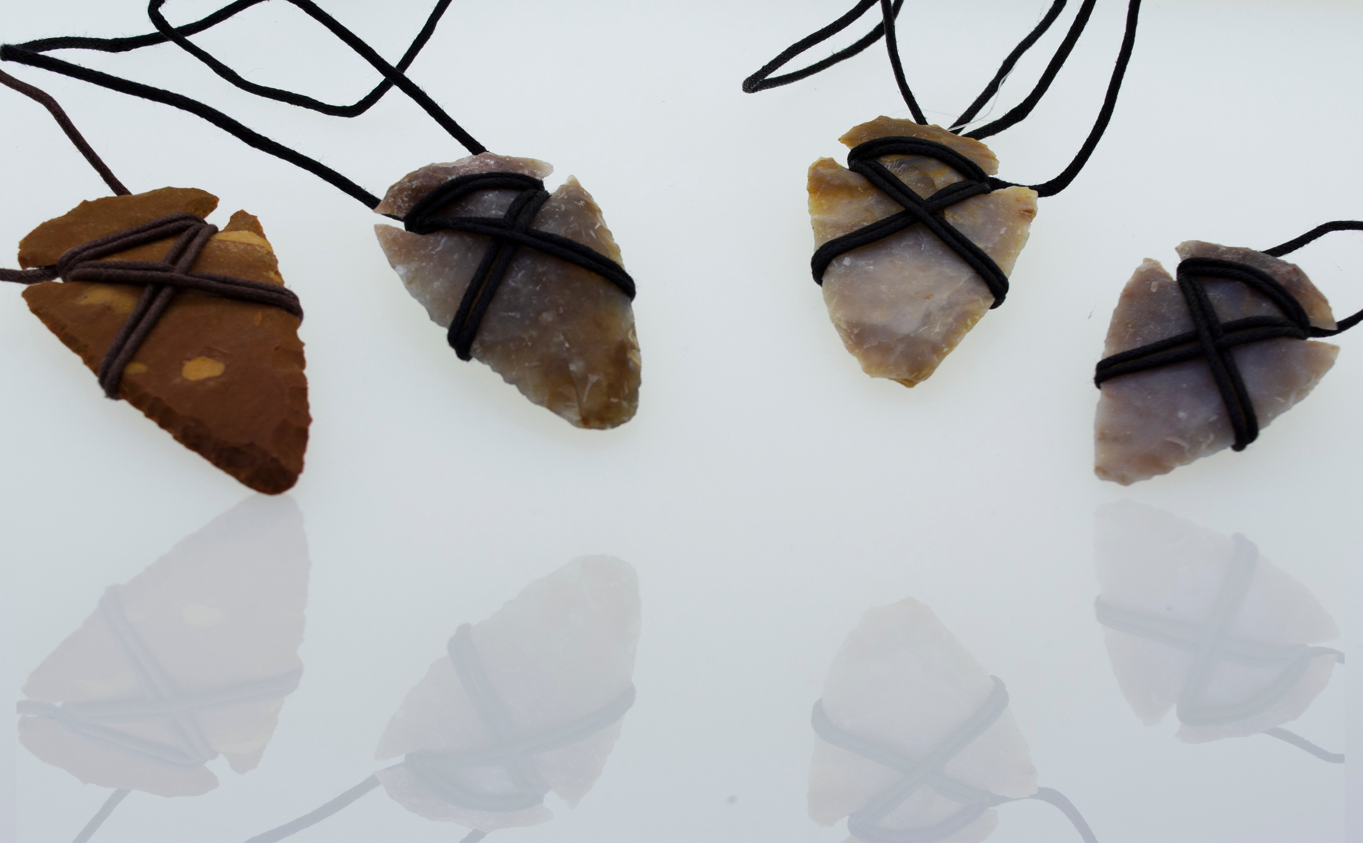 A group of Super Silver Arrowhead Necklaces with Cord on a white surface.